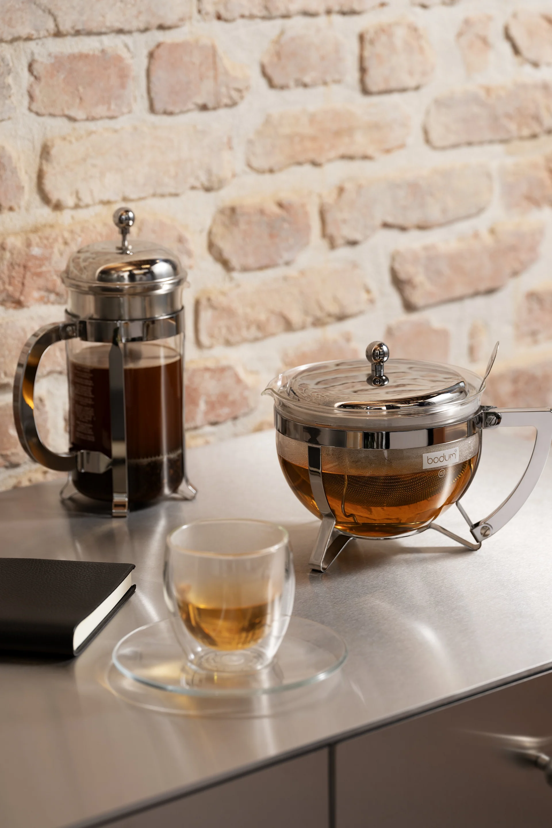 Cadeau pour la Saint-Valentin : ici, une cafetière à piston et une théière de la collection Chambord de Bodum sont posées à côté d'une tasse Bistro remplie de thé sur un buffet de cuisine.