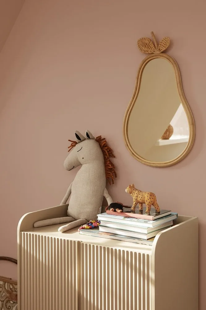 Le coussin Safari cheval de Ferm Living est assis sur une commode dans une chambre d'enfant, à côté duquel est suspendu le miroir Pear.