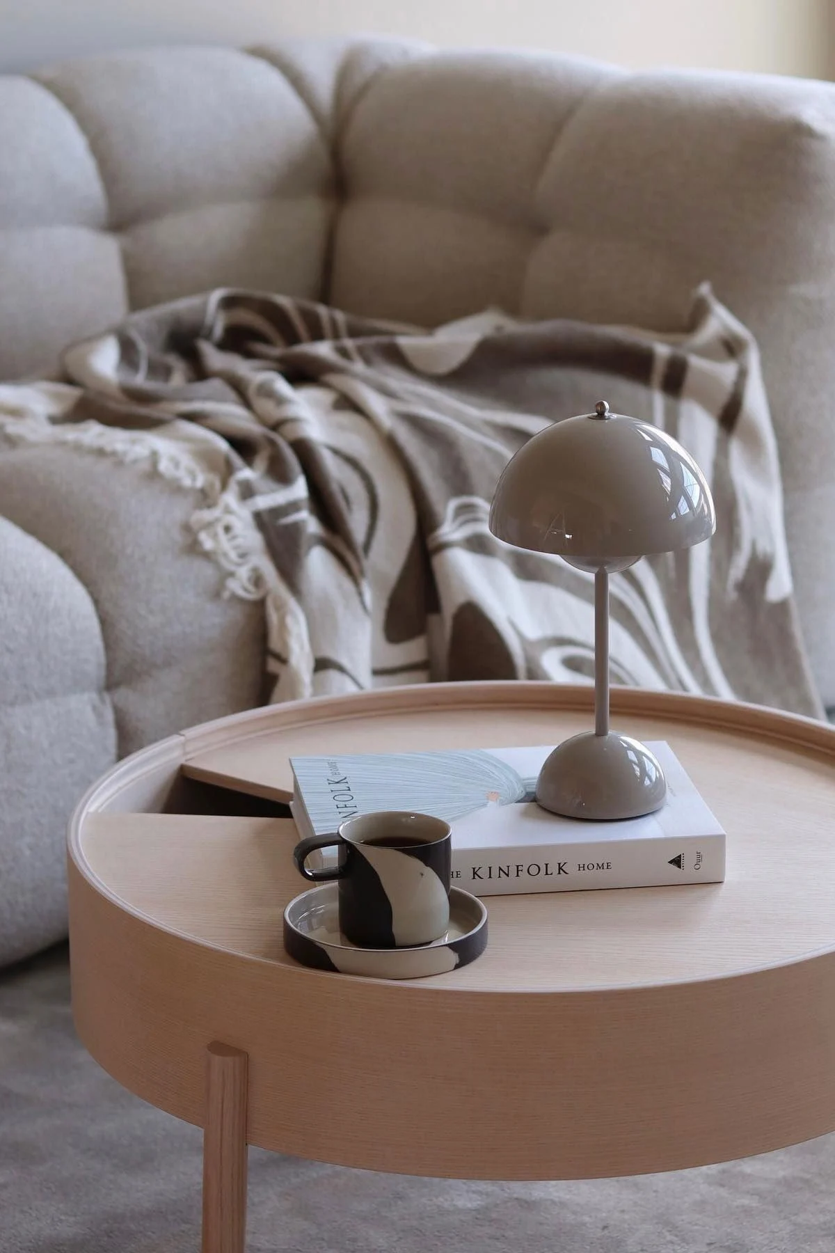 Une table basse en bois décorée avec un livre, une lampe de table Flowerpot de &Tradition et la tasse Inlay de Ferm Living.