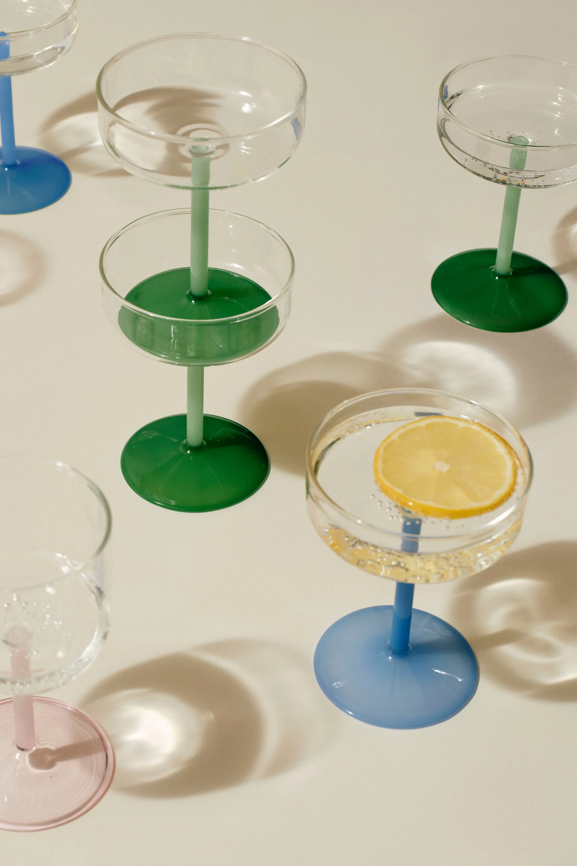 Assortiment de coupes avec des pieds et des bases colorés. Une coupe contient une tranche de citron dans de l'eau pétillante.