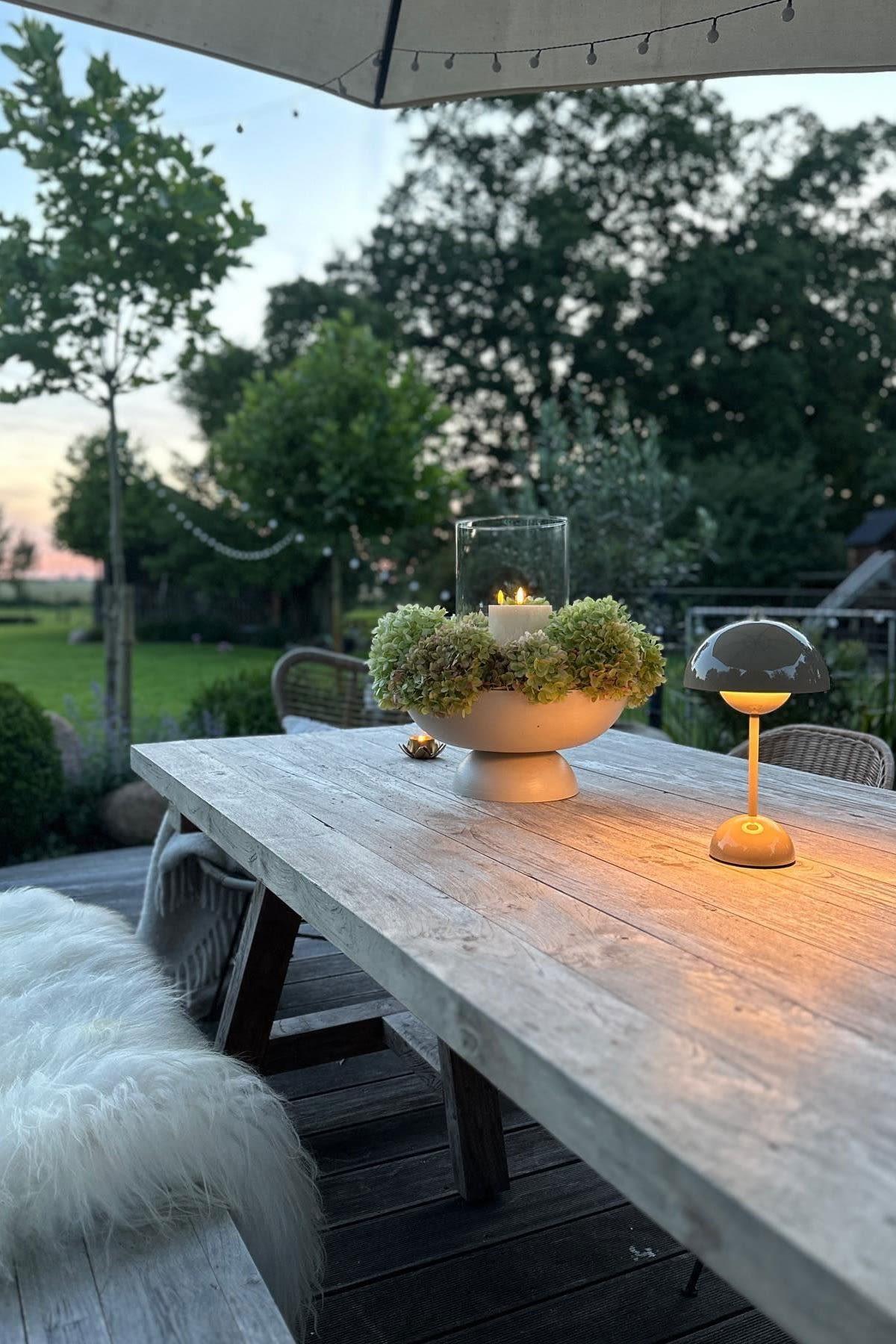 Une terrasse accueillante avec une grande table à manger et des bancs, décorée de bougies et d'une lampe de table Flowerpot de &Tradition.