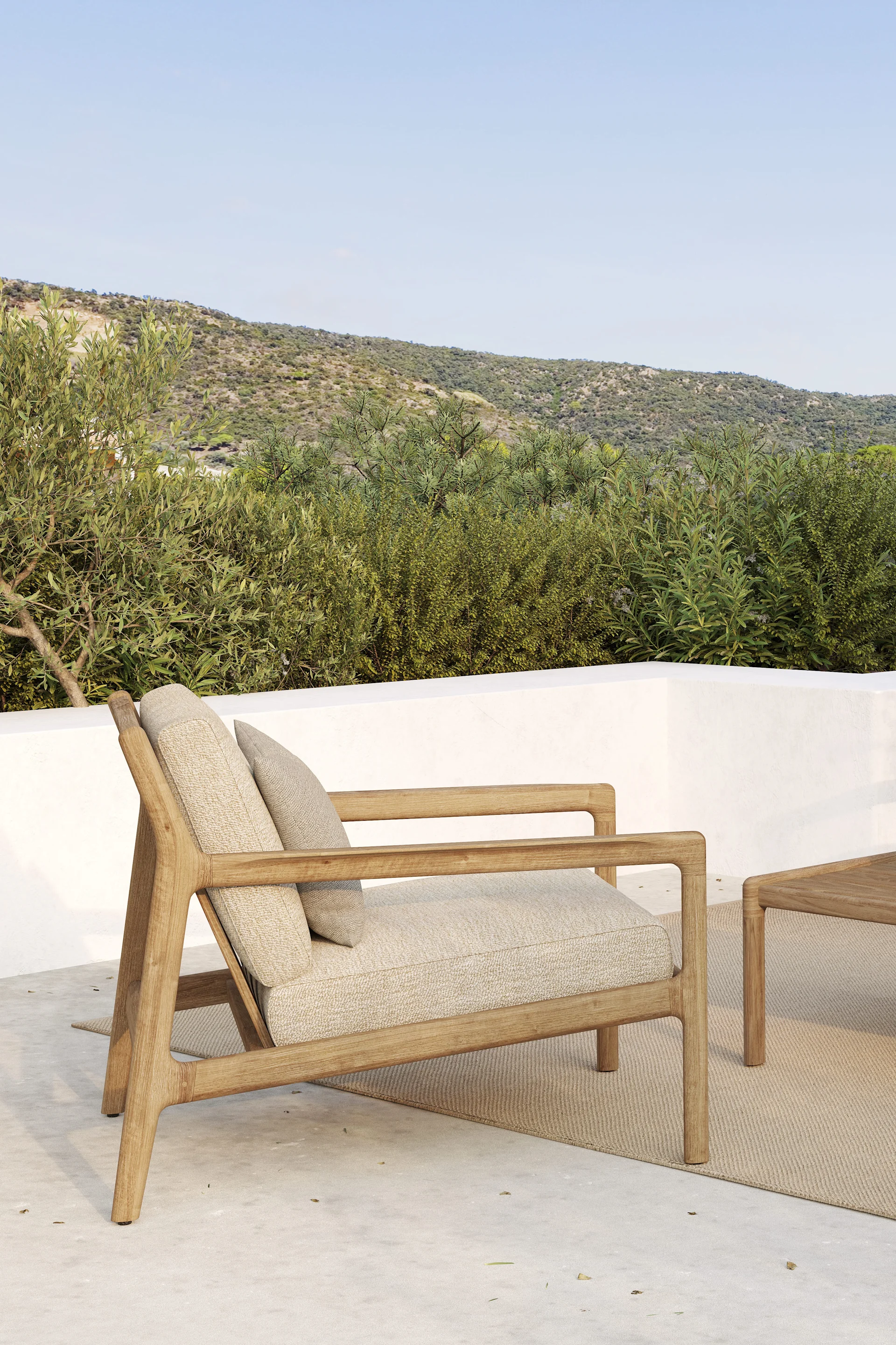 Fauteuil d'extérieur en bois avec coussins clairs sur une terrasse, devant des collines vertes et un ciel bleu.