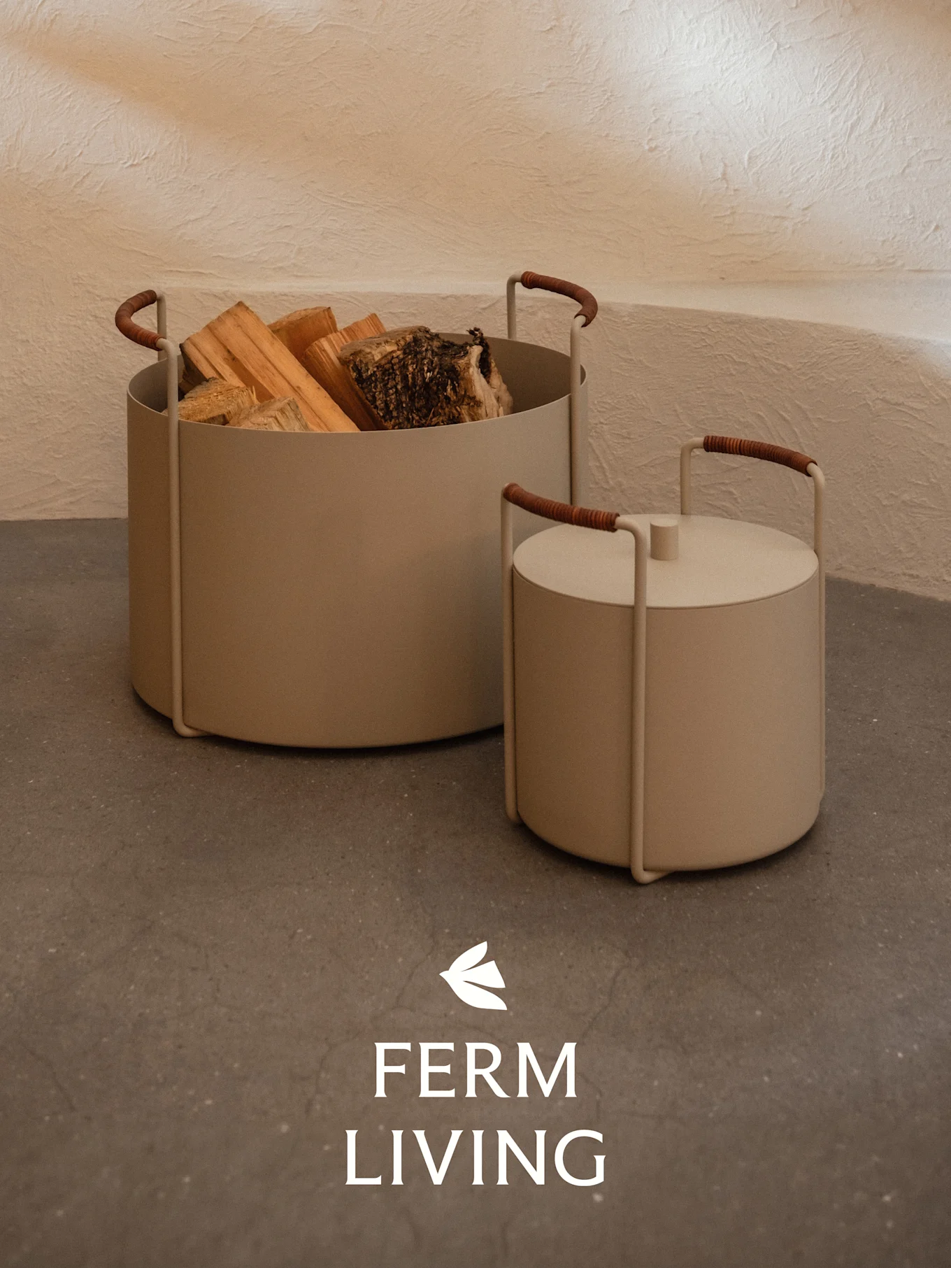 Deux récipients cylindriques beiges, l'un contenant du bois de chauffage et l'autre couvert, avec des poignées gainées de marron sur un sol en béton.