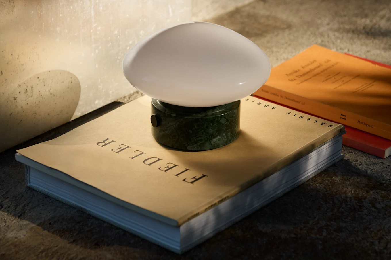 Une lampe de table bleu foncé en forme de champignon, avec une tige et une base argentées, posée sur une table réfléchissante à côté de livres.