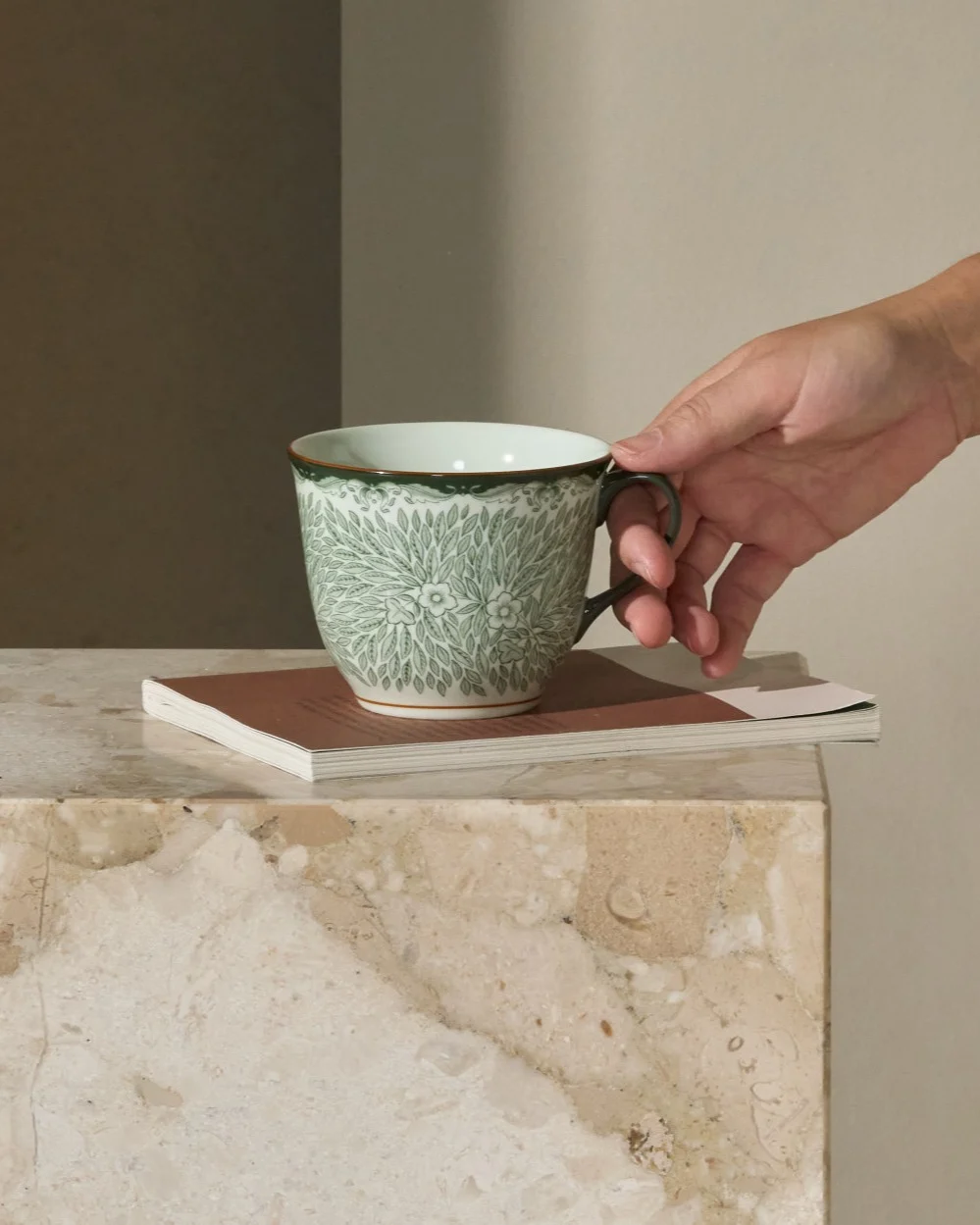 Personne attrapant une tasse verte à motifs sur une table d'appoint en marbre à côté d'un canapé.