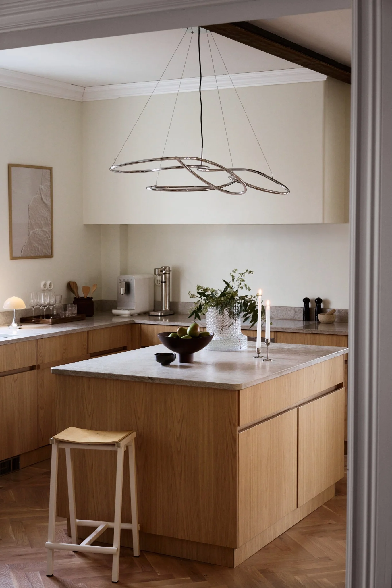 Cuisine moderne avec des armoires en bois clair, des comptoirs en marbre, un grand îlot et un lustre chromé sculptural.