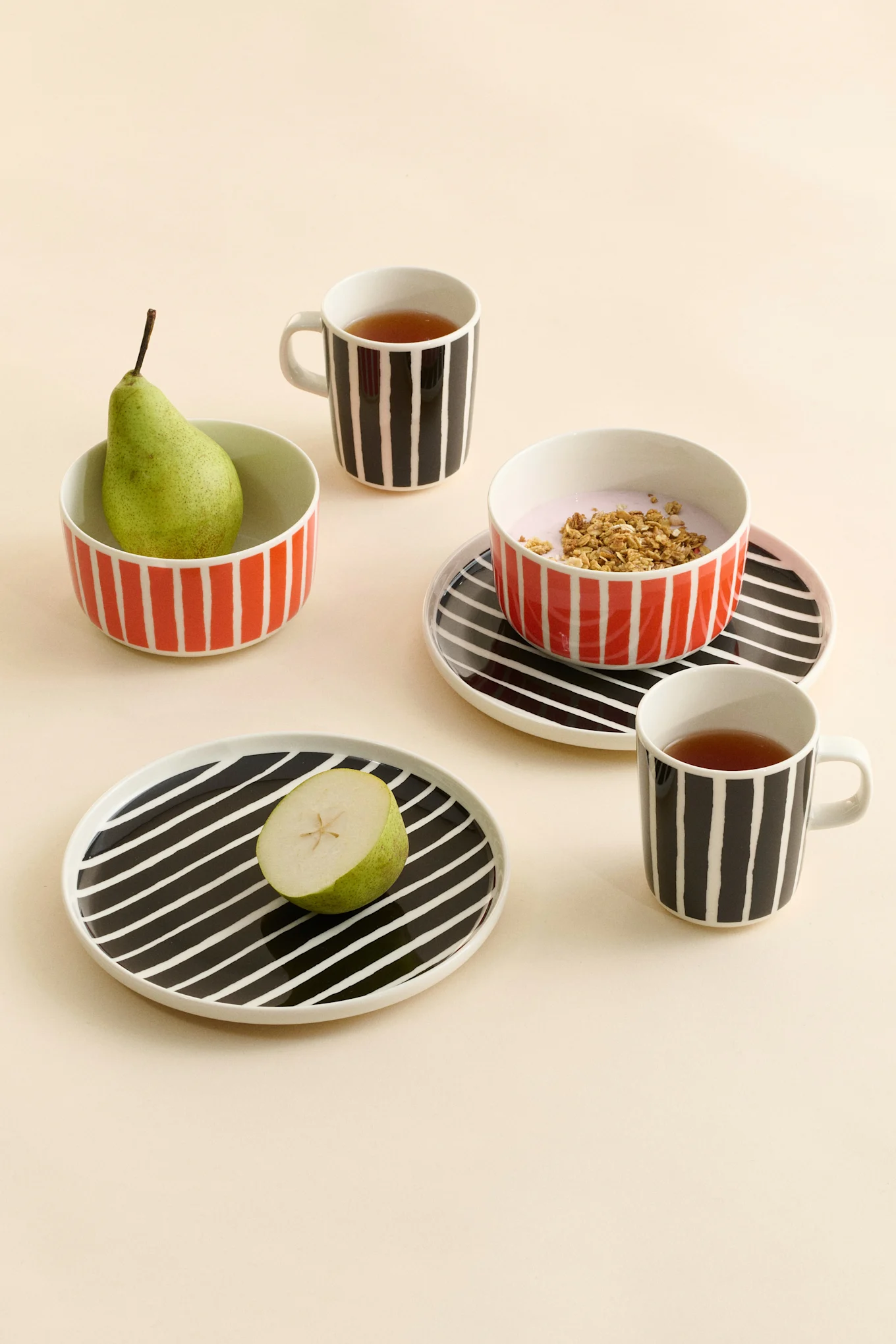 Mugs, bols et assiettes en céramique rayés avec du thé, une poire, du yaourt et du granola.