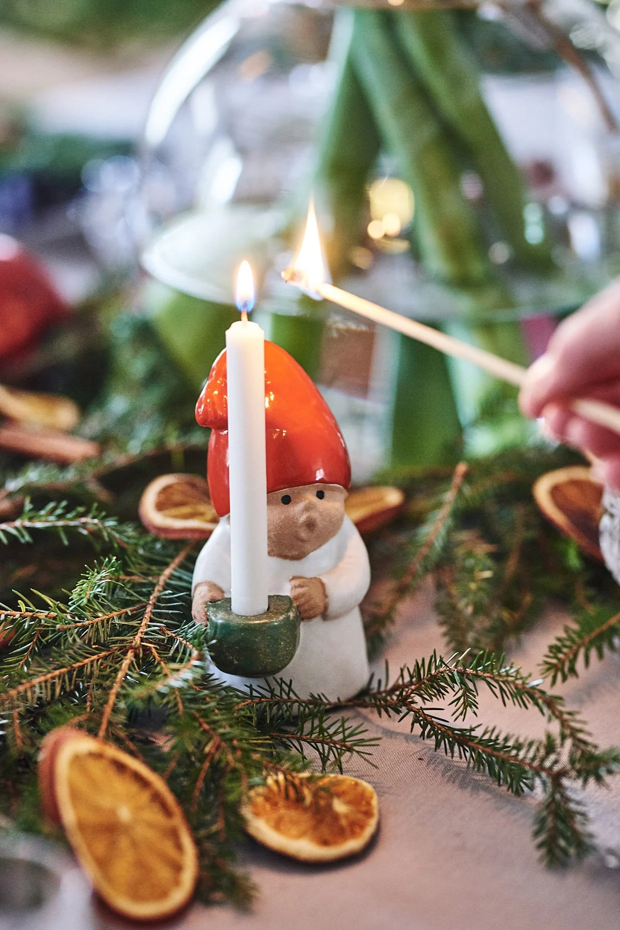 Noël en Suède : le Tomte se présente sous différentes formes. Ici, il apparaît sous la forme d'une petite figurine en céramique posée sur une table dressée pour Noël, tandis que la bougie qu'il tient dans la main vient d'être allumée.