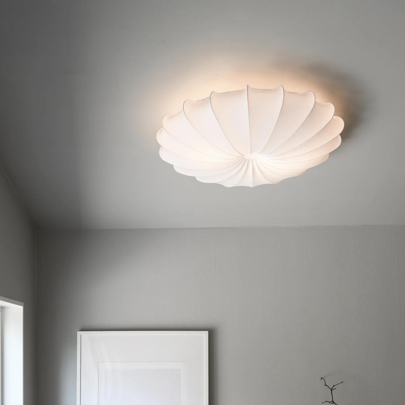 Un plafonnier blanc, plissé et en forme de coquille illumine un plafond gris.