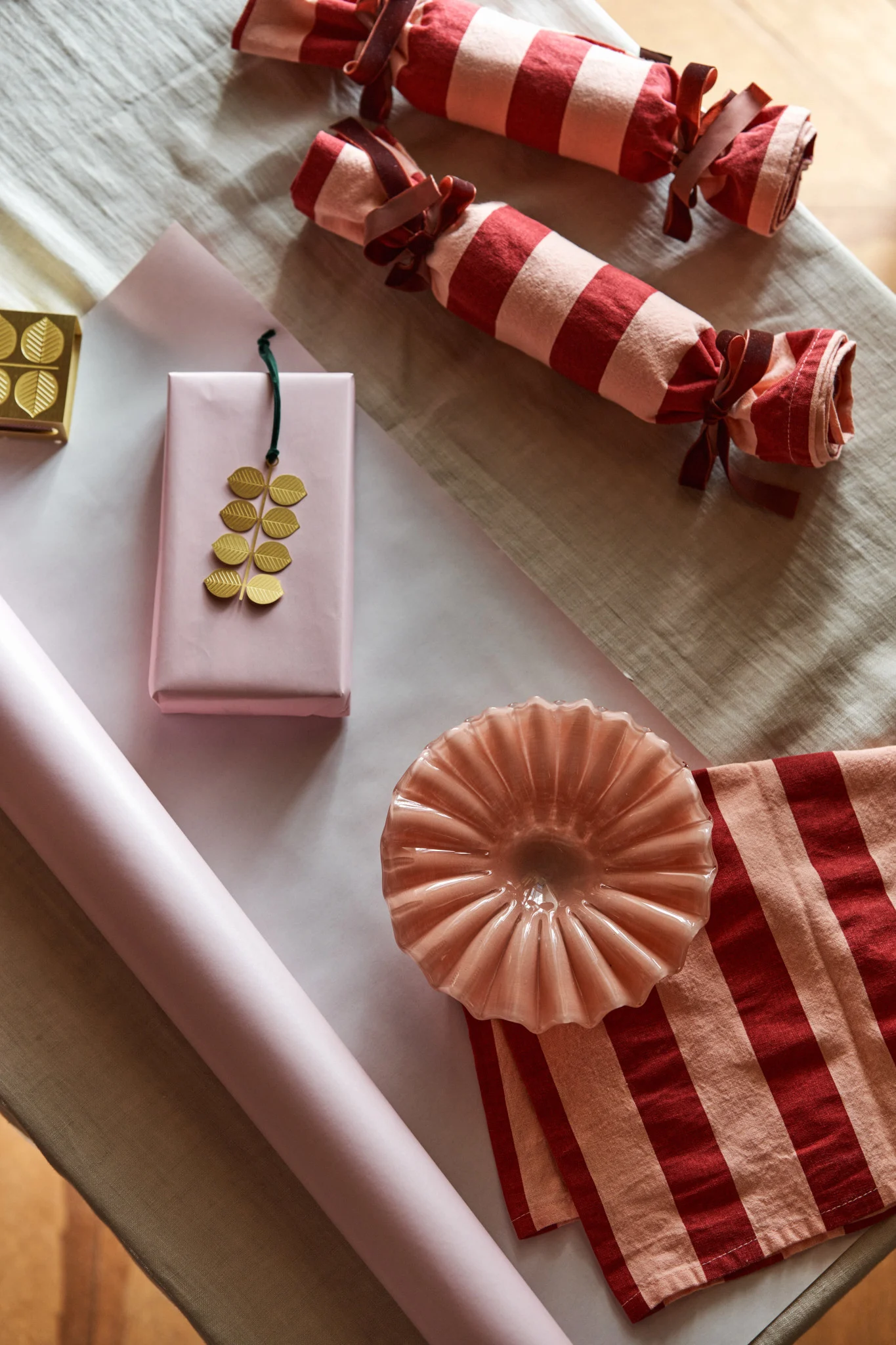 Ici, un bol rose de Byon et un pendentif doré de Pluto attendent d’être joliment emballés dans des torchons rayés et du papier rose – une manière créative de célébrer le premier Avent.
