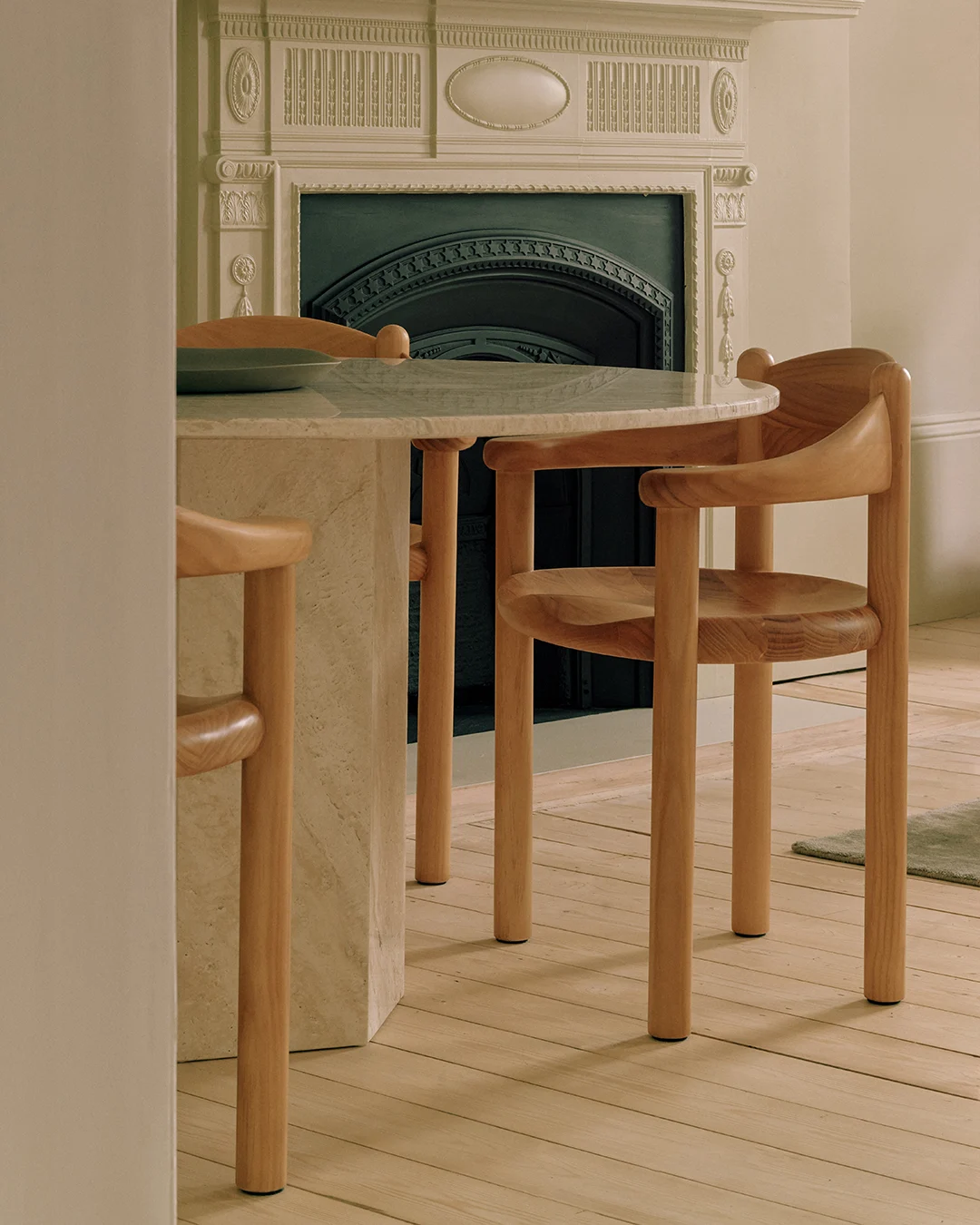 Une table ronde en marbre avec deux chaises en bois clair, devant une cheminée décorative.