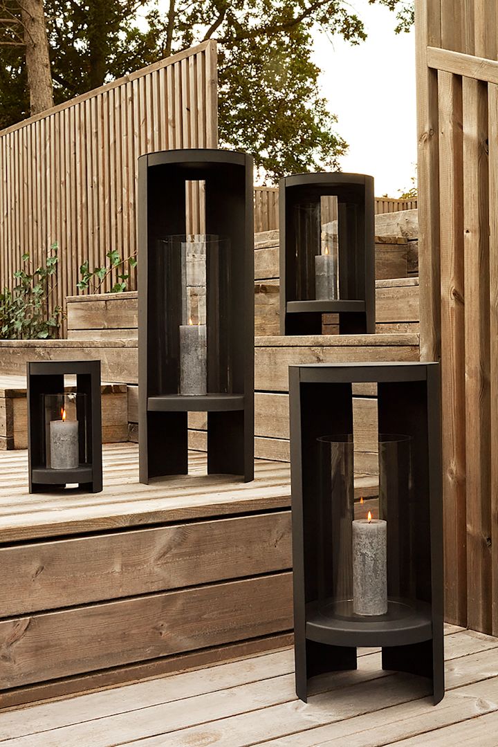 Lanternes et photophores pour l'extérieur - ici, vous voyez la lanterne Oro d'AYTM en noir et en différentes tailles posée sur un escalier en bois dans un jardin.