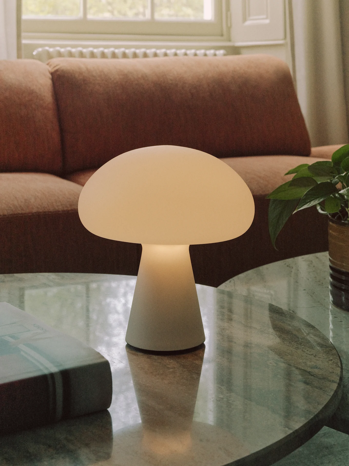 Une lampe de table blanche cassée en forme de champignon sur une table basse ronde en marbre dans un salon.