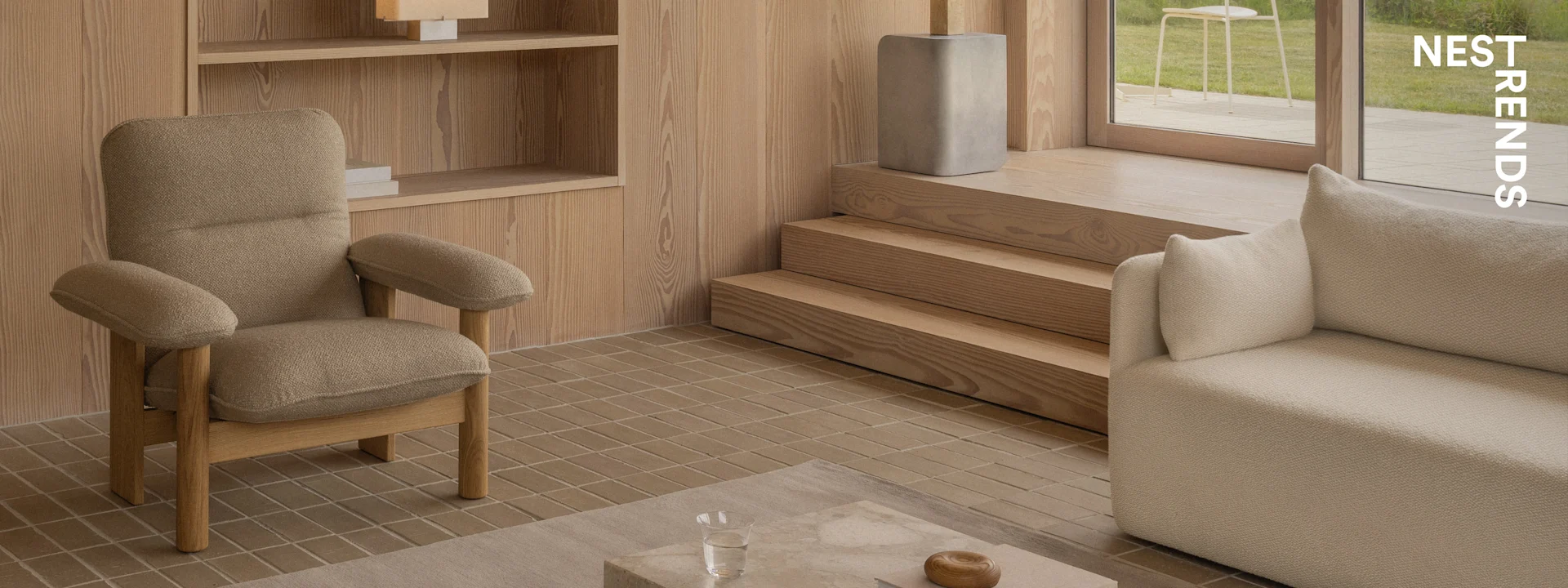 Un salon moderne avec un fauteuil marron texturé, un canapé beige, des panneaux muraux en bois, un sol carrelé et une vue sur un jardin.