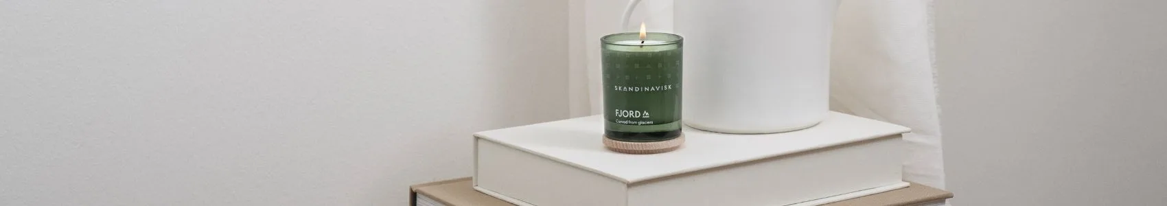 Un livre intitulé 'NOTES FROM THE FELLS' sur une couverture grise à côté de deux bougies de style scandinave, l'une noire et allumée, l'autre marron avec un couvercle en bois.