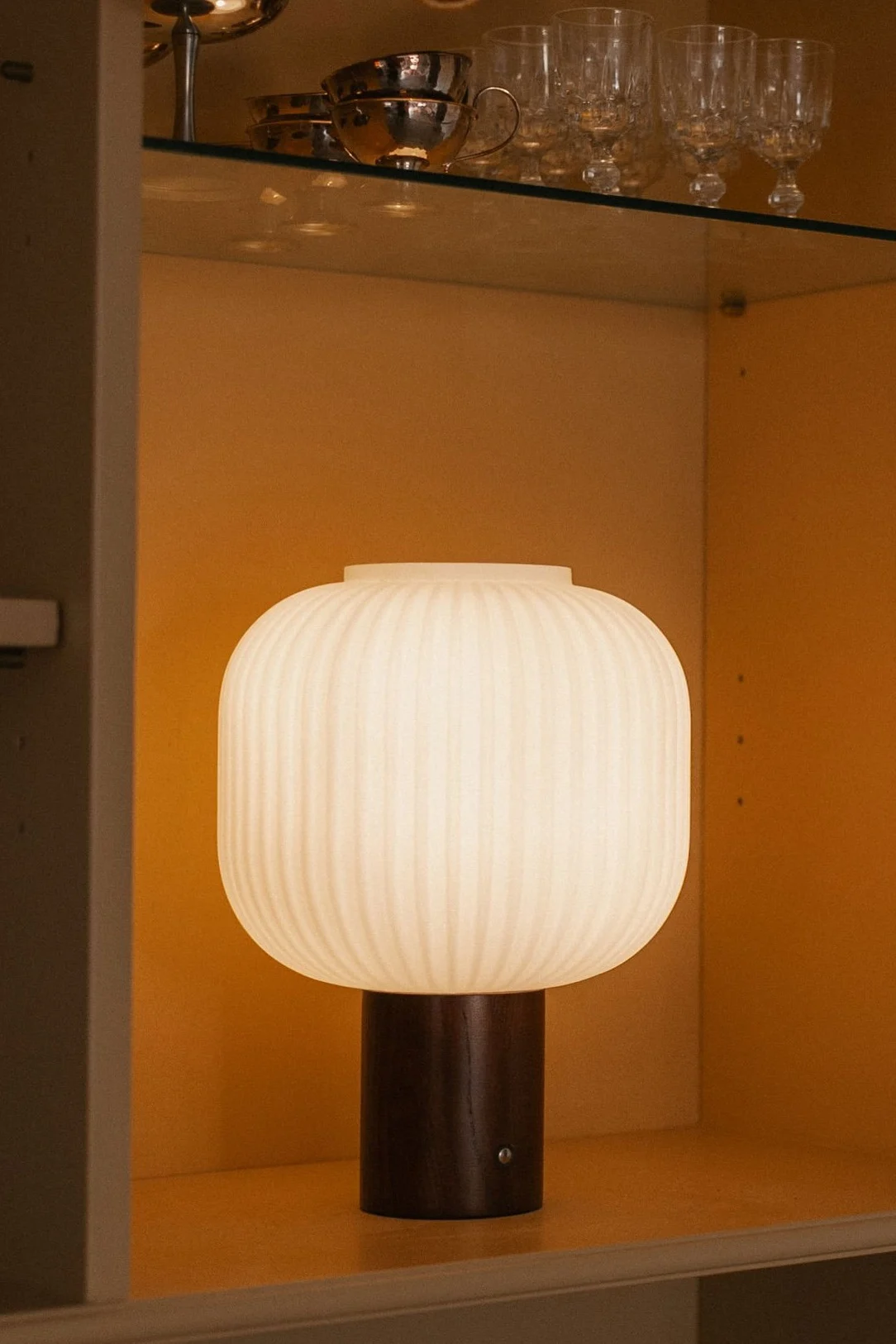 Lampe de table blanche côtelée lumineuse avec une base en bois foncé, sous une guirlande d'oranges séchées.