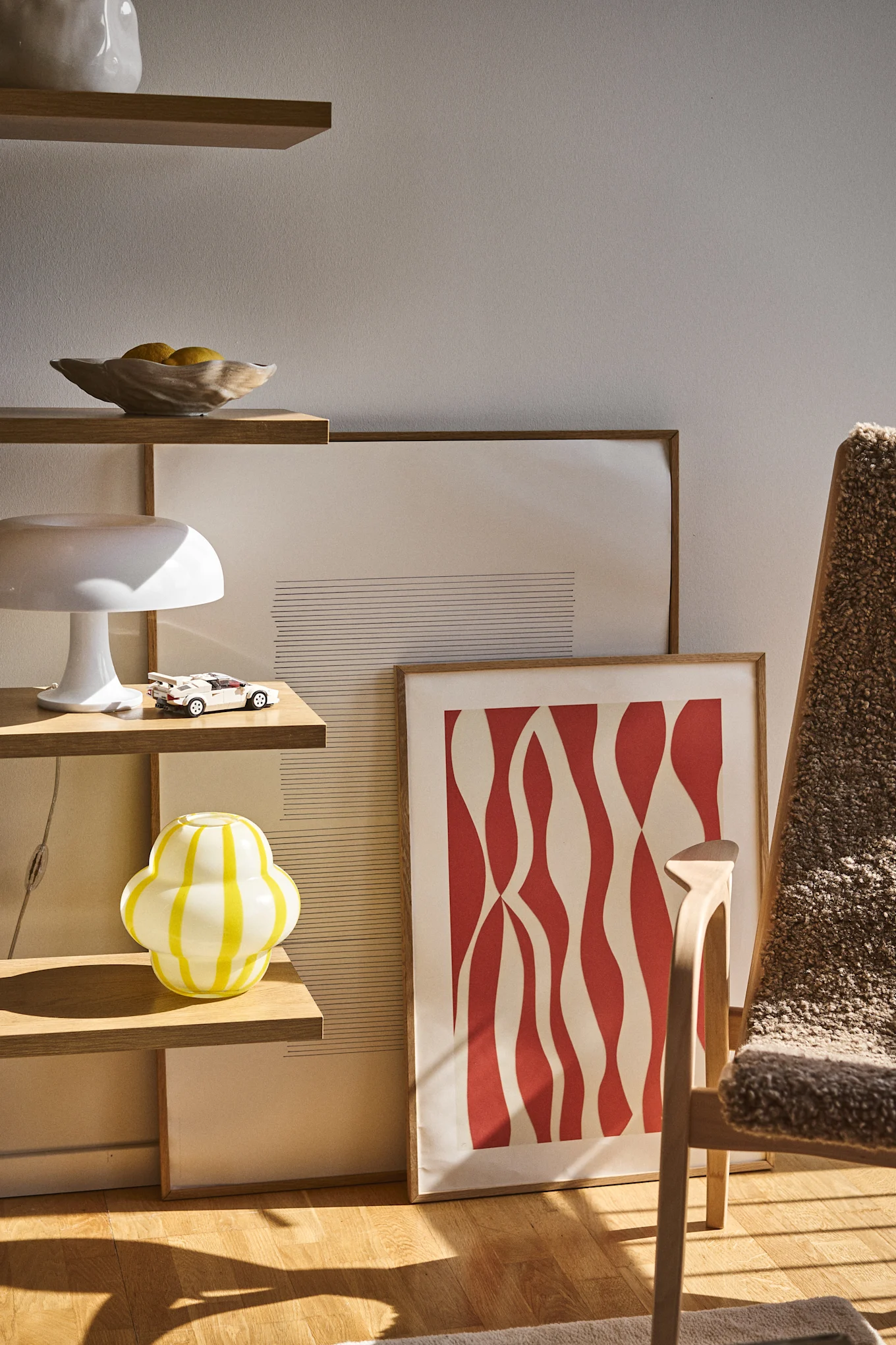 Le vase Curlie de Byon a un design rond et bulbeux en verre rayé jaune et blanc. Il est ici placé dans une bibliothèque ouverte avec le bol Shell, des lampes et des tableaux.