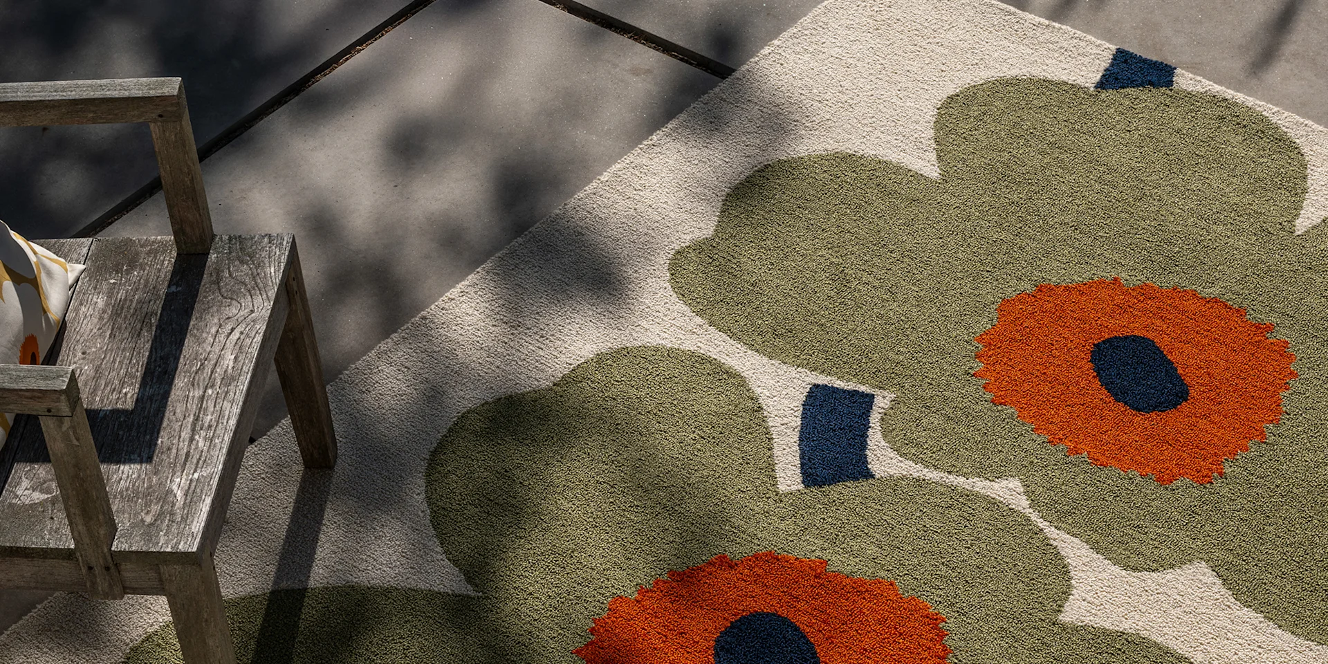 Tapis d'extérieur floral vert olive et orange à côté d'une chaise en bois patiné sur un patio en béton.