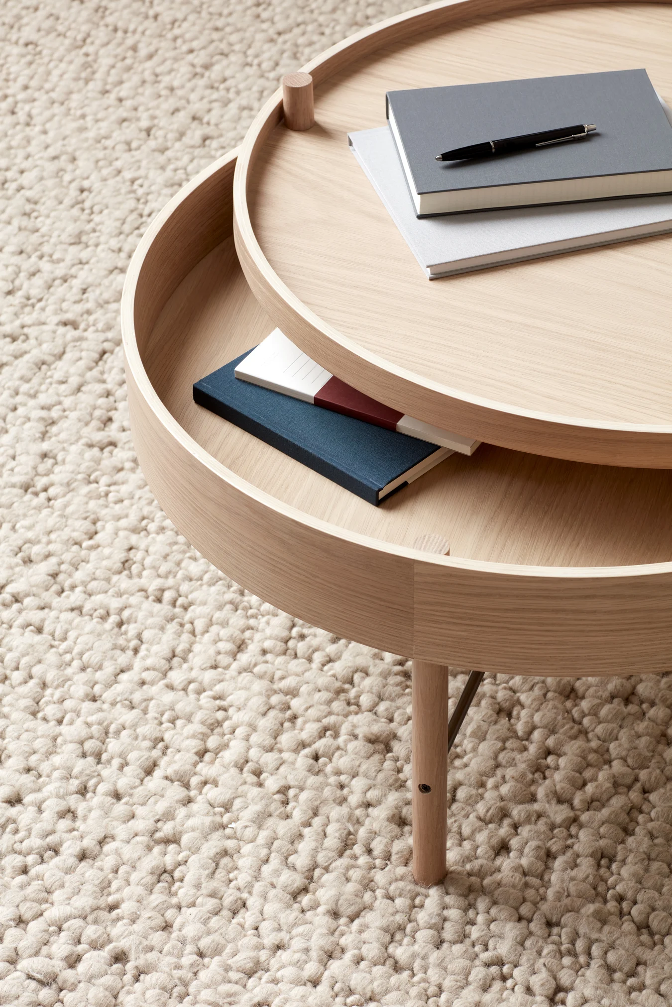 Sur un tapis clair se trouve la table d'appoint en bois Turning table d'Audo Copenhagen, qui impressionne par sa fonctionnalité et son espace de rangement.
