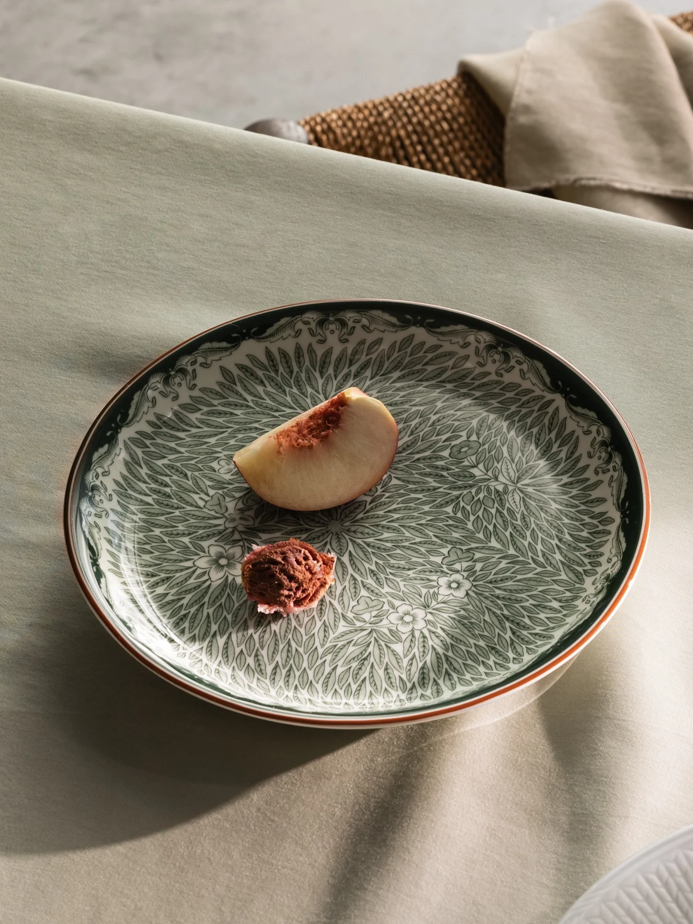 Une table dressée avec une assiette verte à motifs contenant une tranche de pêche, et une vue partielle d'une assiette blanche avec de la crème et des tranches de pêche.