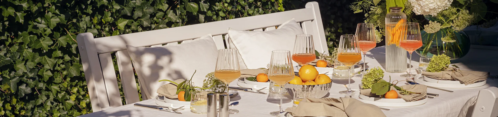 Table extérieure dressée pour un repas d'été avec des assiettes blanches cannelées, des serviettes en lin, des verres cannelés, citrons et mandarines.