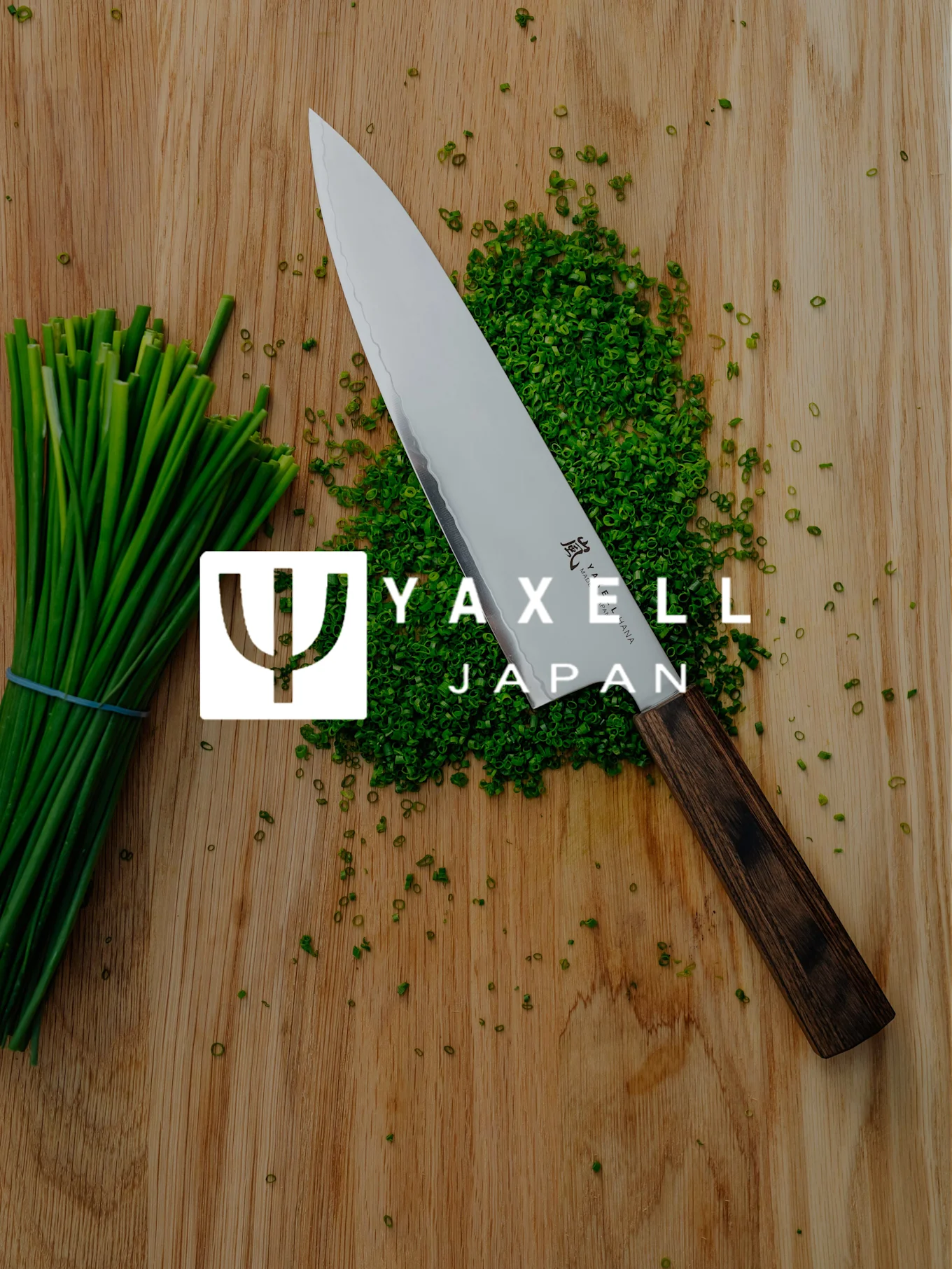 Couteau de chef Yaxell, ciboulette hachée et botte de ciboulette sur planche en bois avec logo Yaxell Japan.