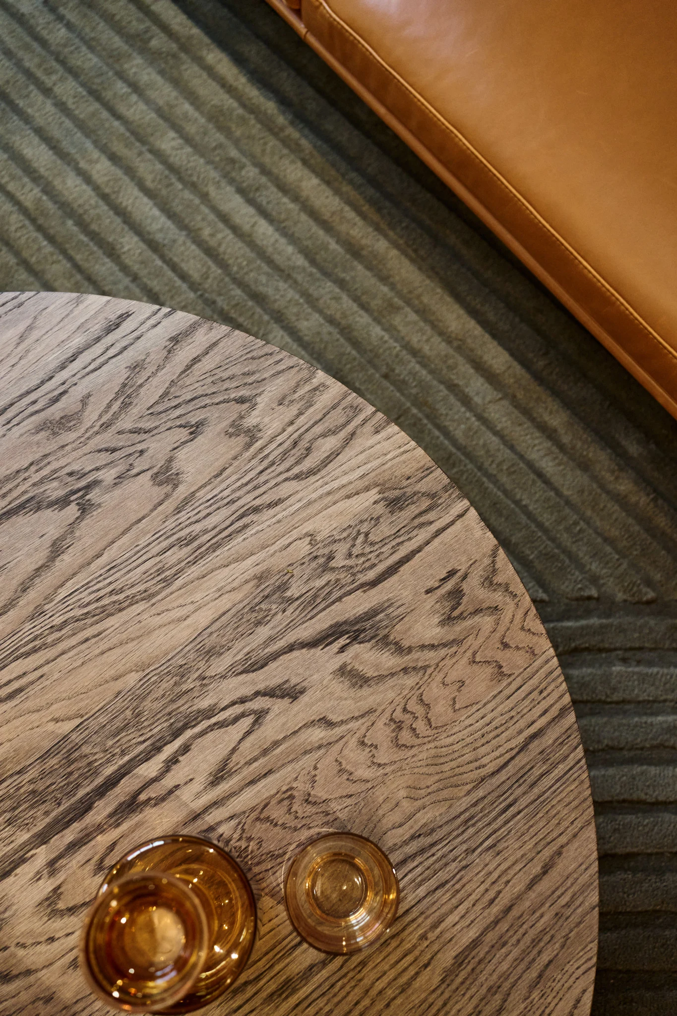 Une table basse au plateau marron foncé se trouve devant un canapé, sur lequel sont posés différents verres ambrés de la collection Raise de Muuto.