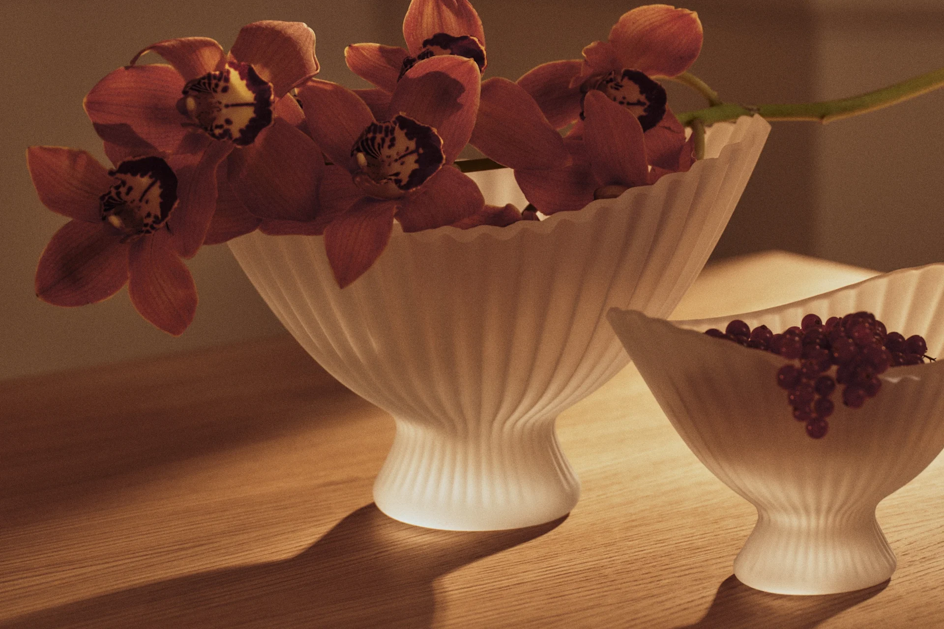 Orchidées rouge-orange dans un vase en verre cannelé et groseilles rouges dans un bol assorti sur table en bois.