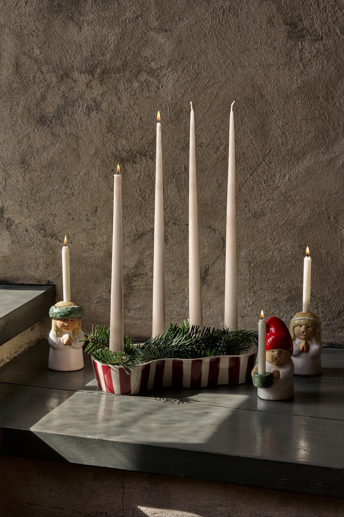 Décoration de l'Avent avec quatre bougies éteintes, du sapin vert et trois figurines tenant des bougies allumées.