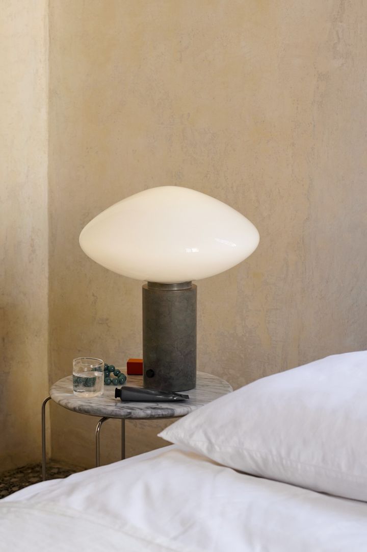 Tendances de la décoration d'intérieur pour l'automne 2025 : La lampe de table Mist avec socle en marbre vert de &tradition est posée sur une table d'appoint à côté du lit.