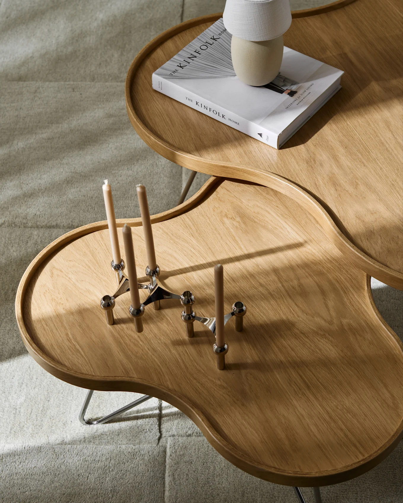 Deux tables basses en bois irrégulières sur tapis gris clair. L'une a un livre et une lampe, l'autre deux bougeoirs avec bougies.