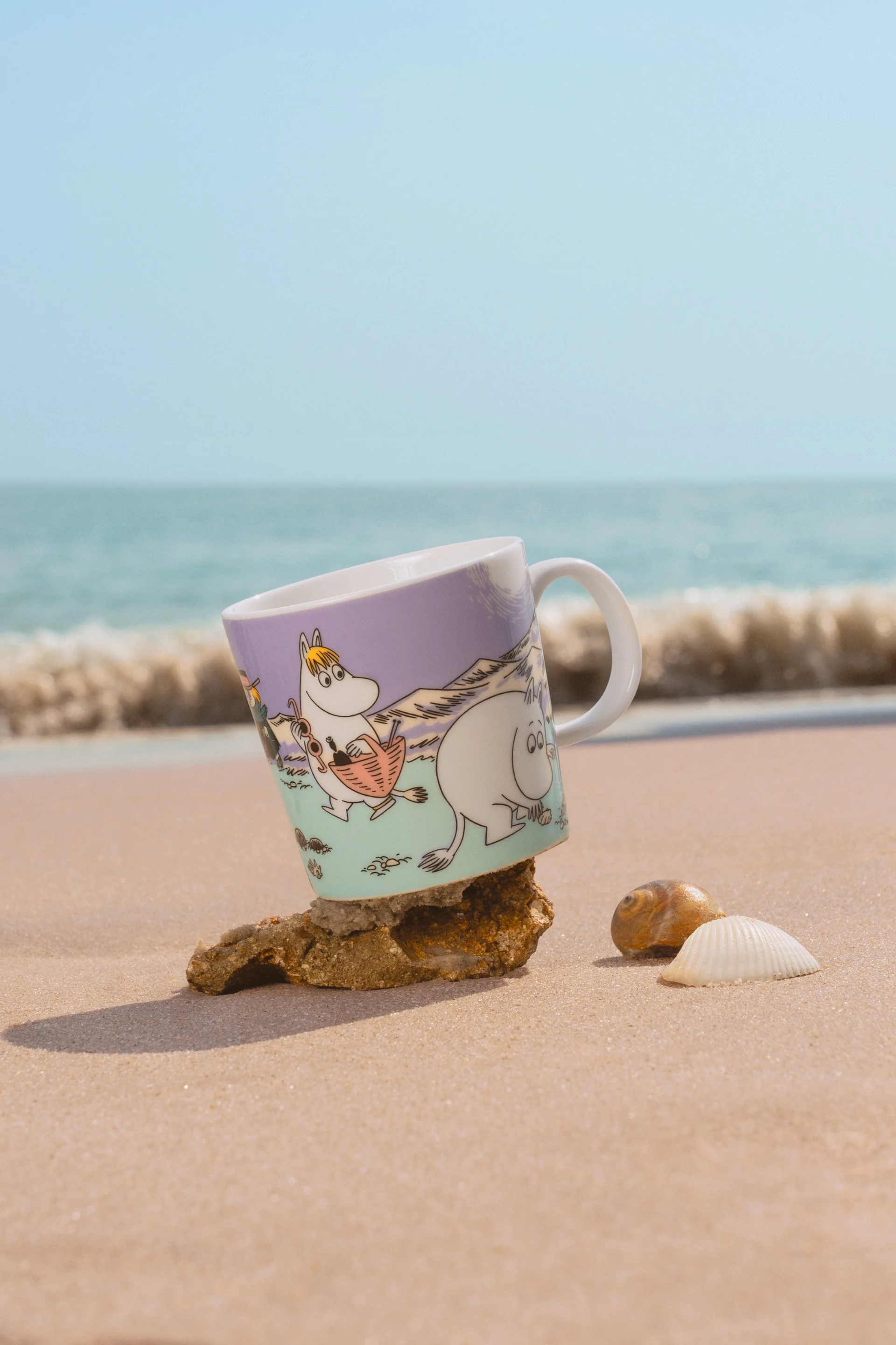 Le mug Moomin Summer 2025, « Beach Day », se trouve sur une plage de sable.