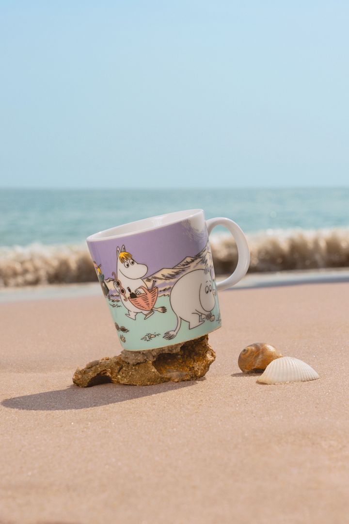 Le mug Moomin Summer 2025, « Beach Day », se trouve sur une plage de sable.