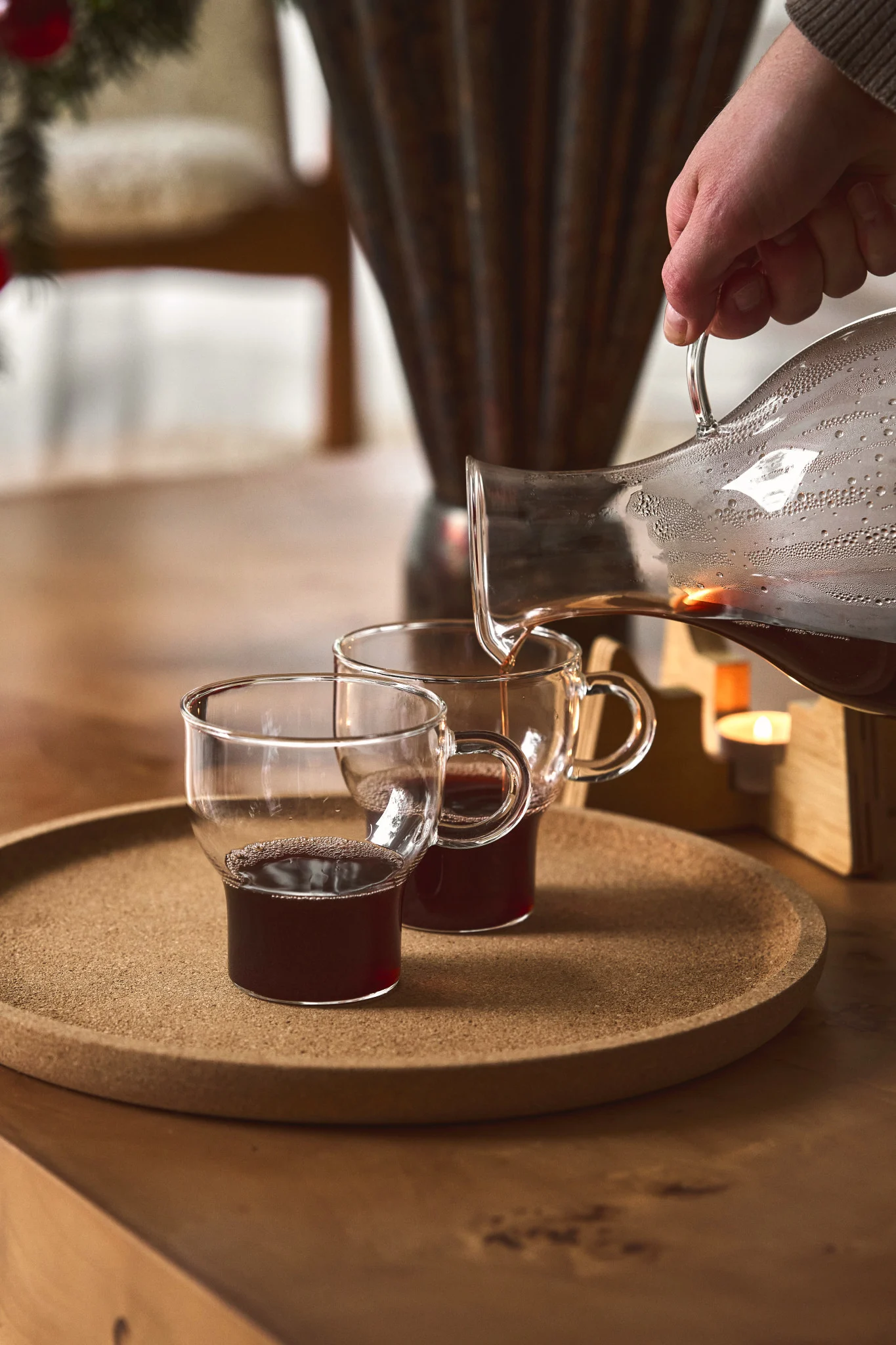 Une personne verse du vin chaud d’une carafe en verre dans une tasse en verre de Sagaform.