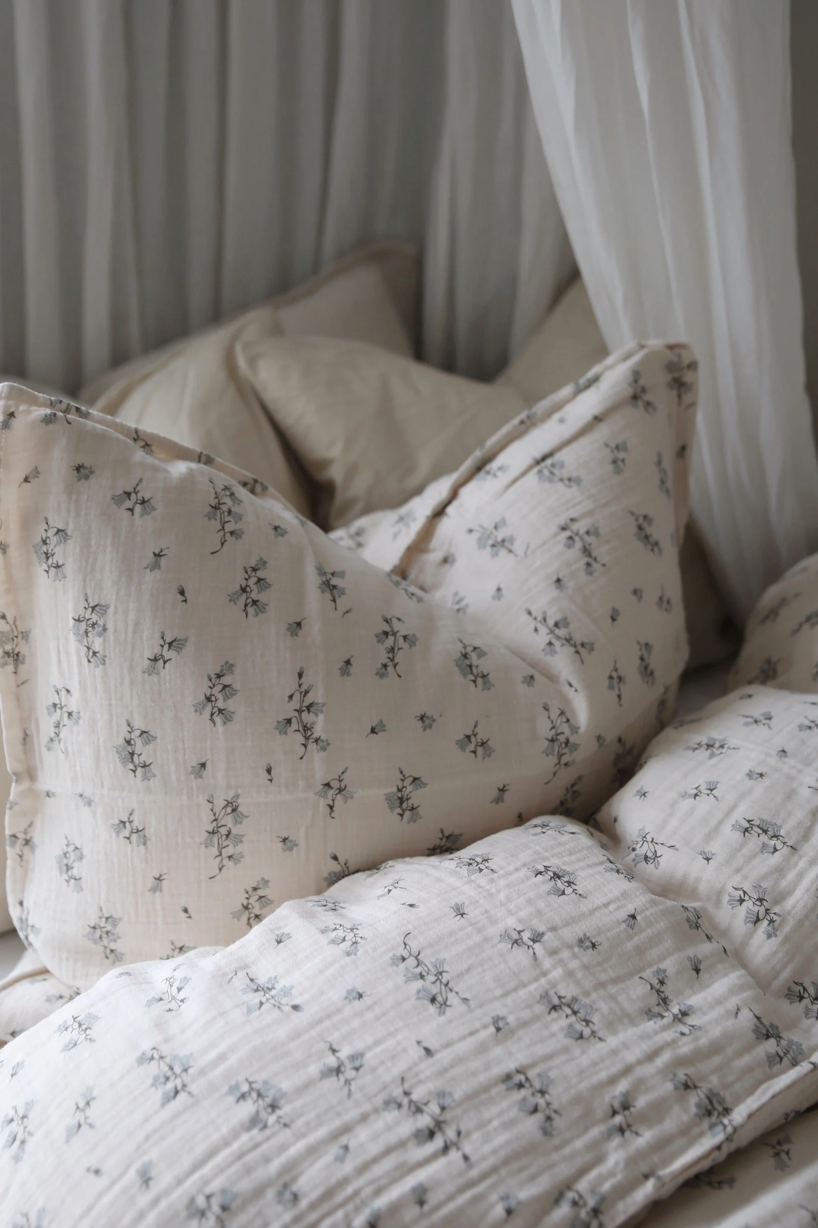 Une parure de lit chaleureuse en tissu froissé beige clair, ornée d'un délicat motif floral bleu et de rideaux blancs.