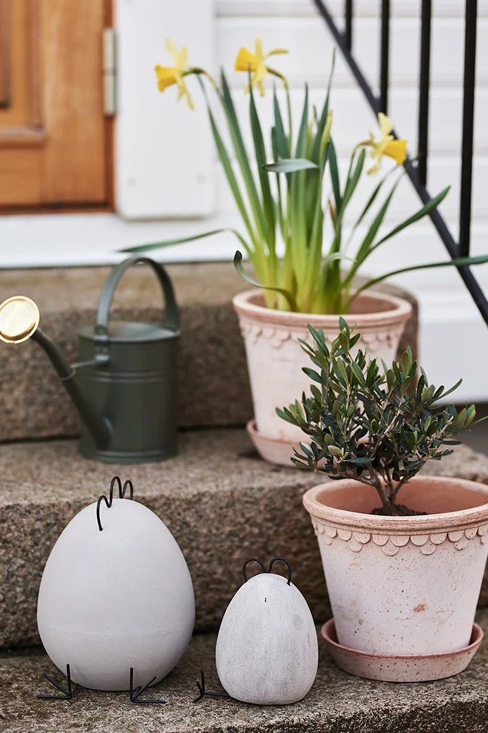 Des poules de Pâques en béton de DBKD sont placées sur l'escalier avec des plantes vertes dans des pots de Bergs Potter. 