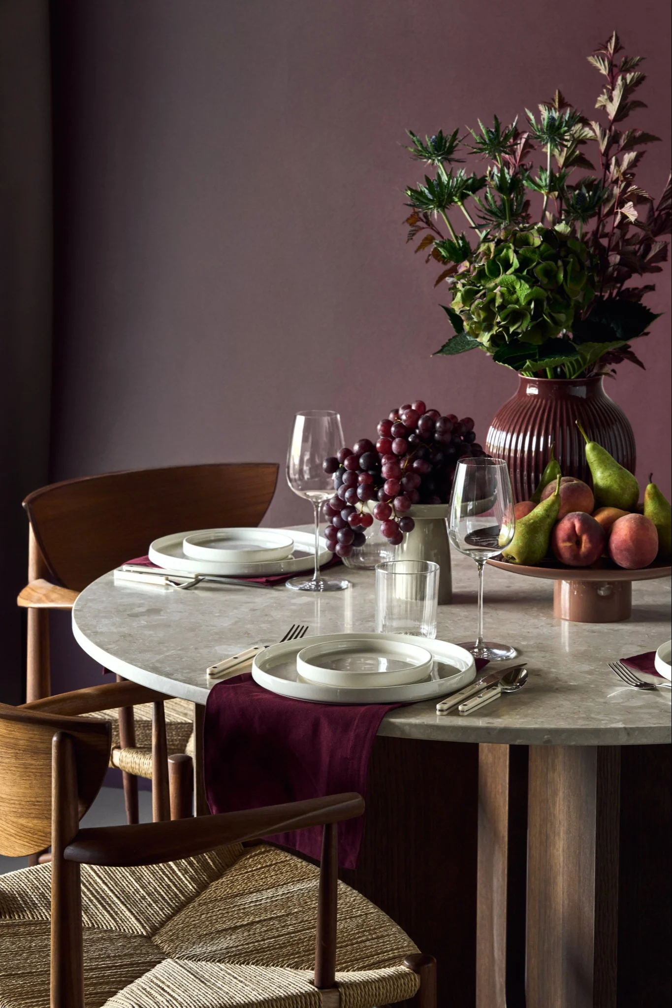 Une table en marbre avec des chaises en bois est dressée avec de la porcelaine blanche et des détails couleur lie-de-vin, parfaitement dans l'air du temps pour les tendances déco 2026.