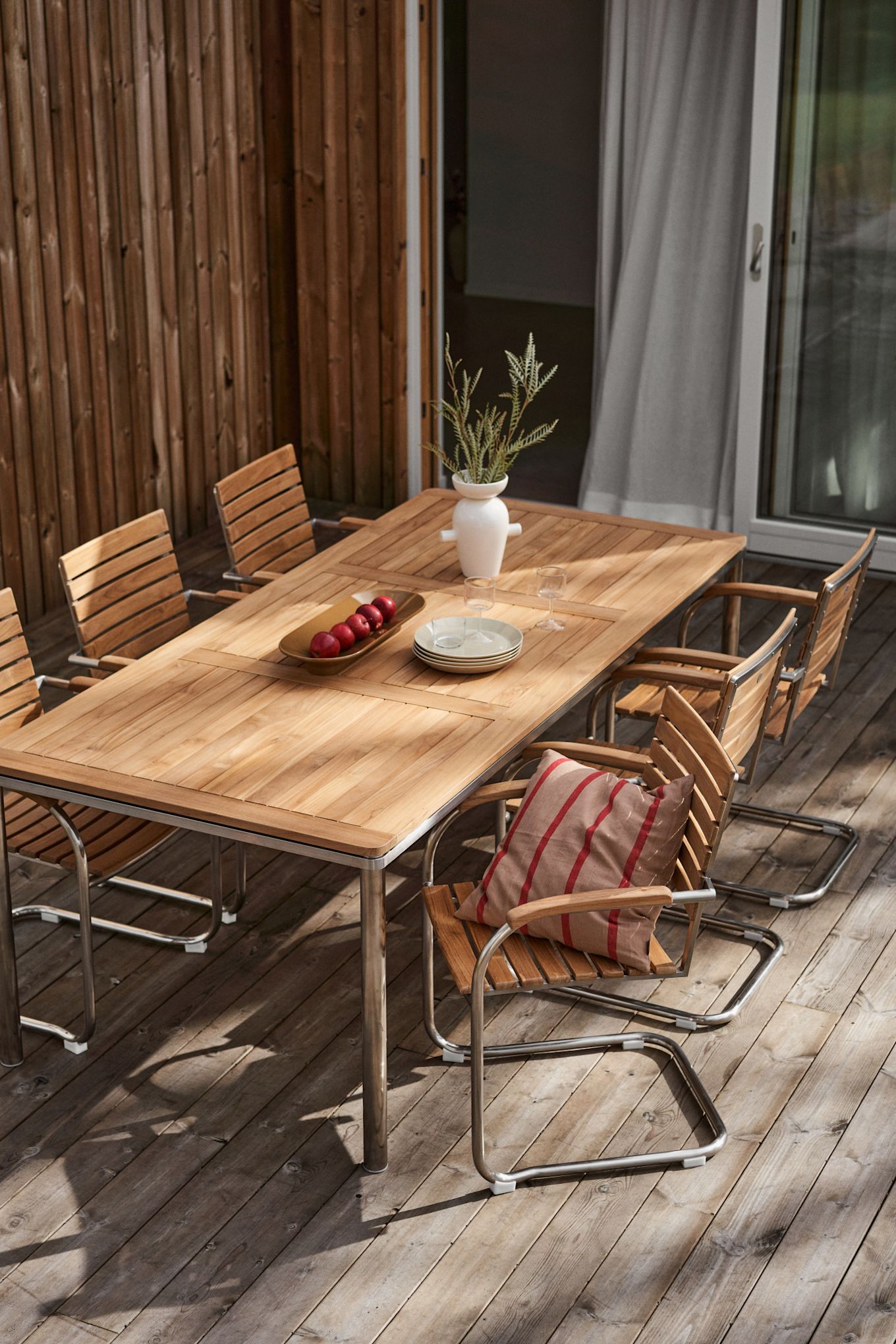 Un patio avec un coin repas confortable, composé de la collection Rörvik de 1898, d'une table décorée d'un vase et d'un coussin sur une chaise.