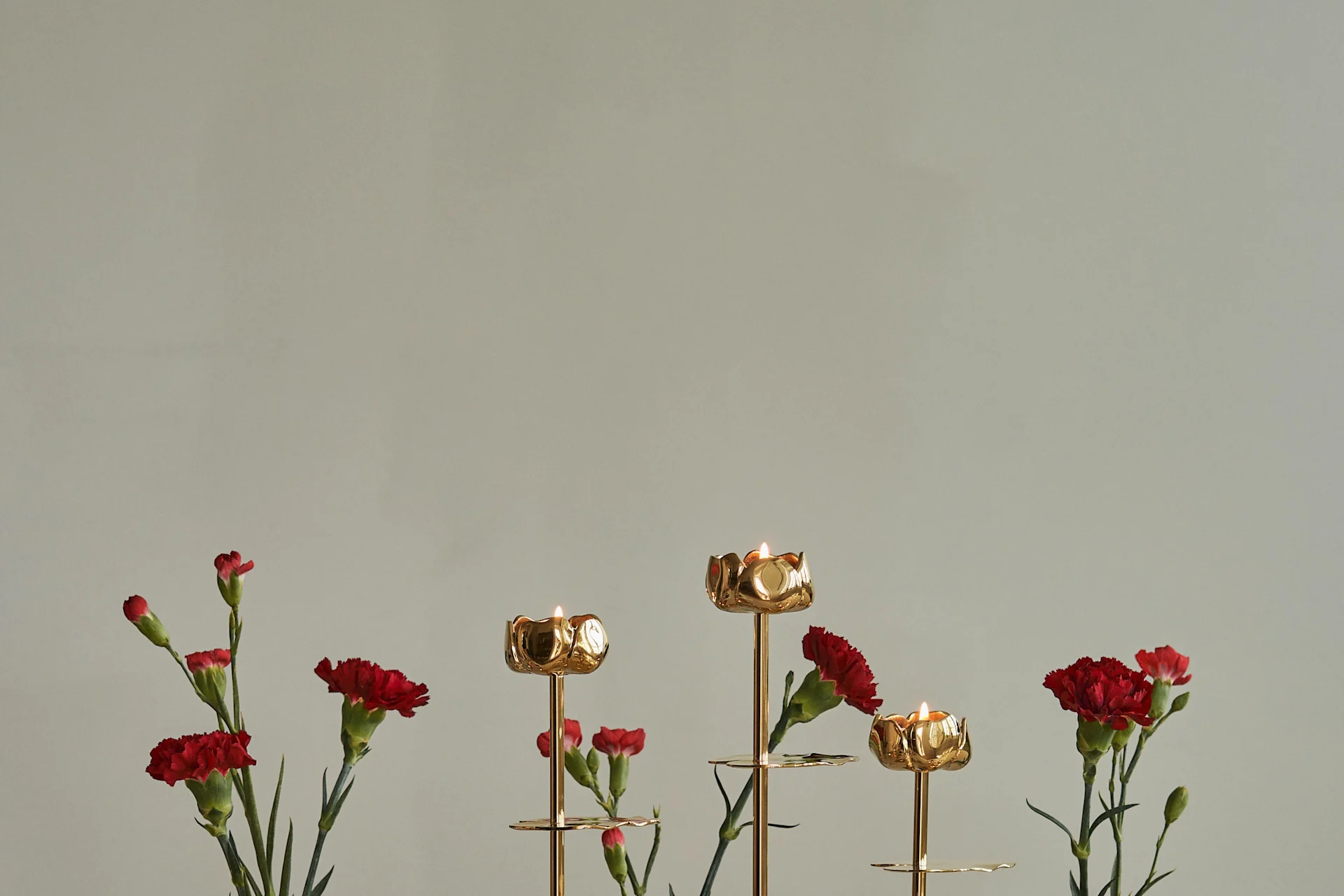 Chandeliers dorés en forme de fleur avec des bougies allumées et des œillets rouges.