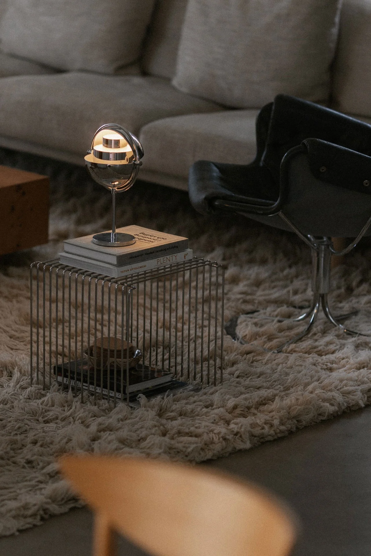Une lampe de table en laiton avec un abat-jour blanc en dôme allumé repose sur un rebord de fenêtre à côté d'un vase blanc avec des branches, avec une vue extérieure.