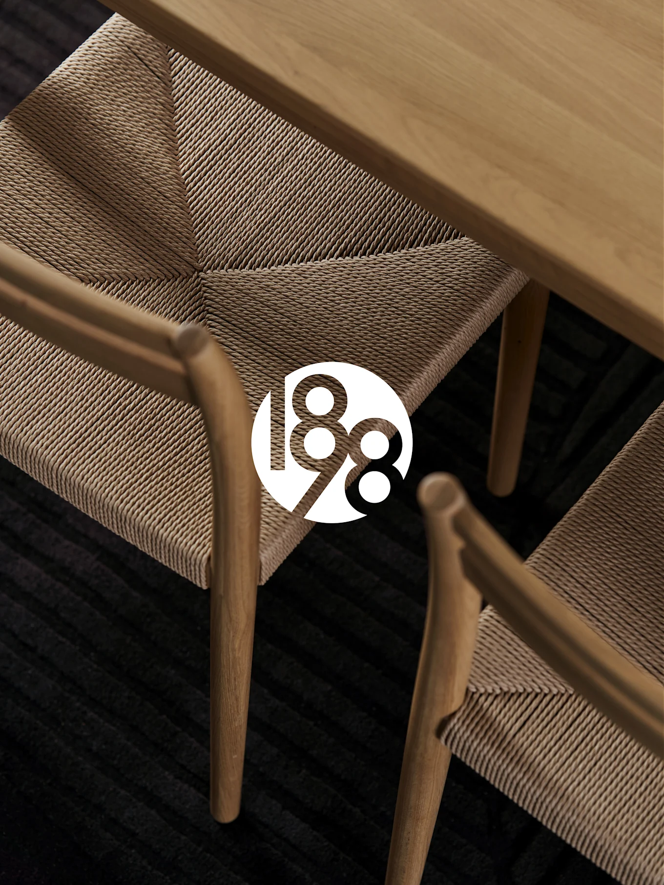 Deux chaises en bois aux sièges tressés, une table en bois et un tapis sombre. Logo blanc '188' en surimpression.