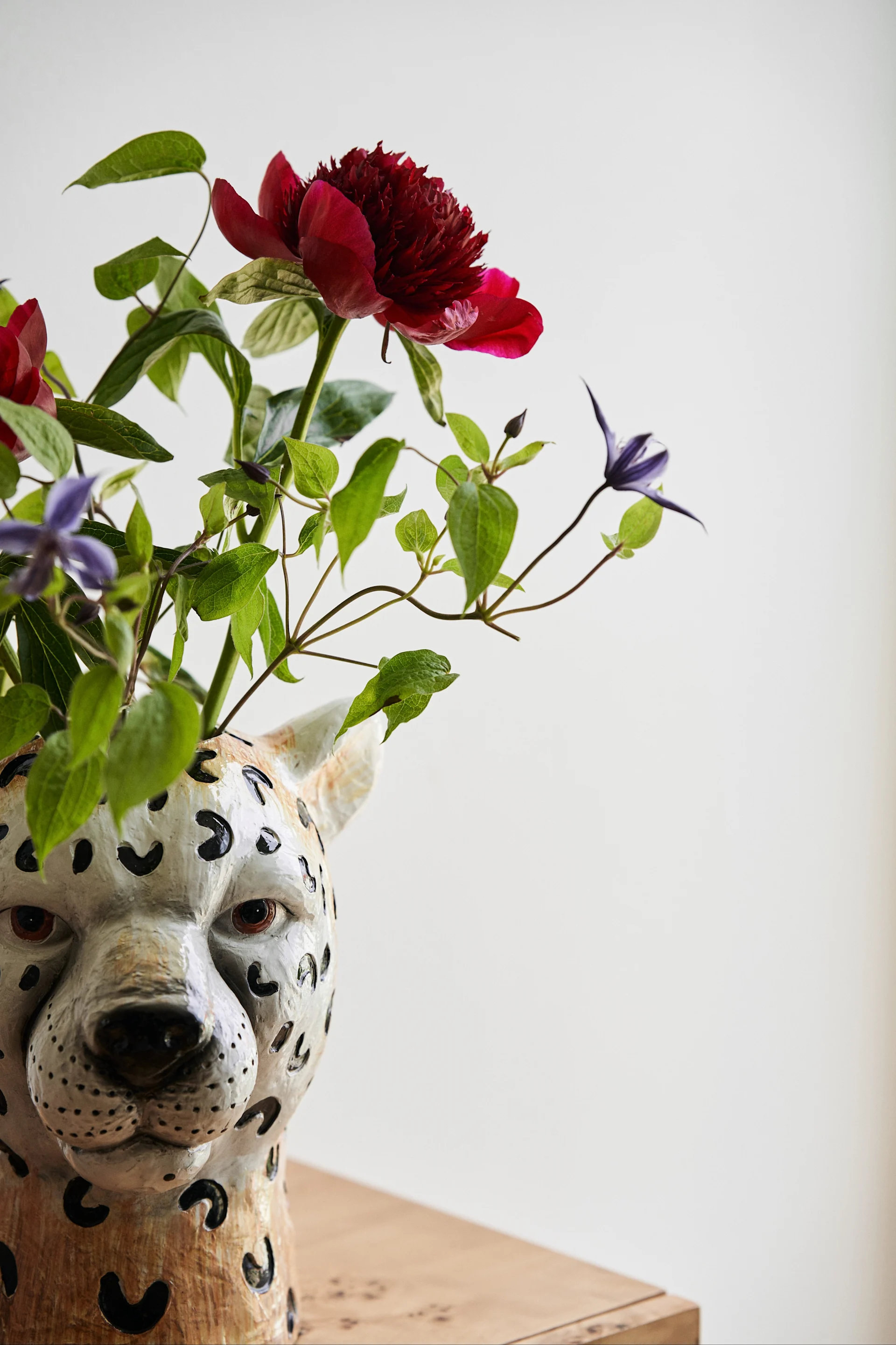 Le vase Guépard de Byon a été le point de départ de la success story de la marque. Voici un gros plan du vase guépard avec un bouquet de fleurs rouge foncé et bleu.