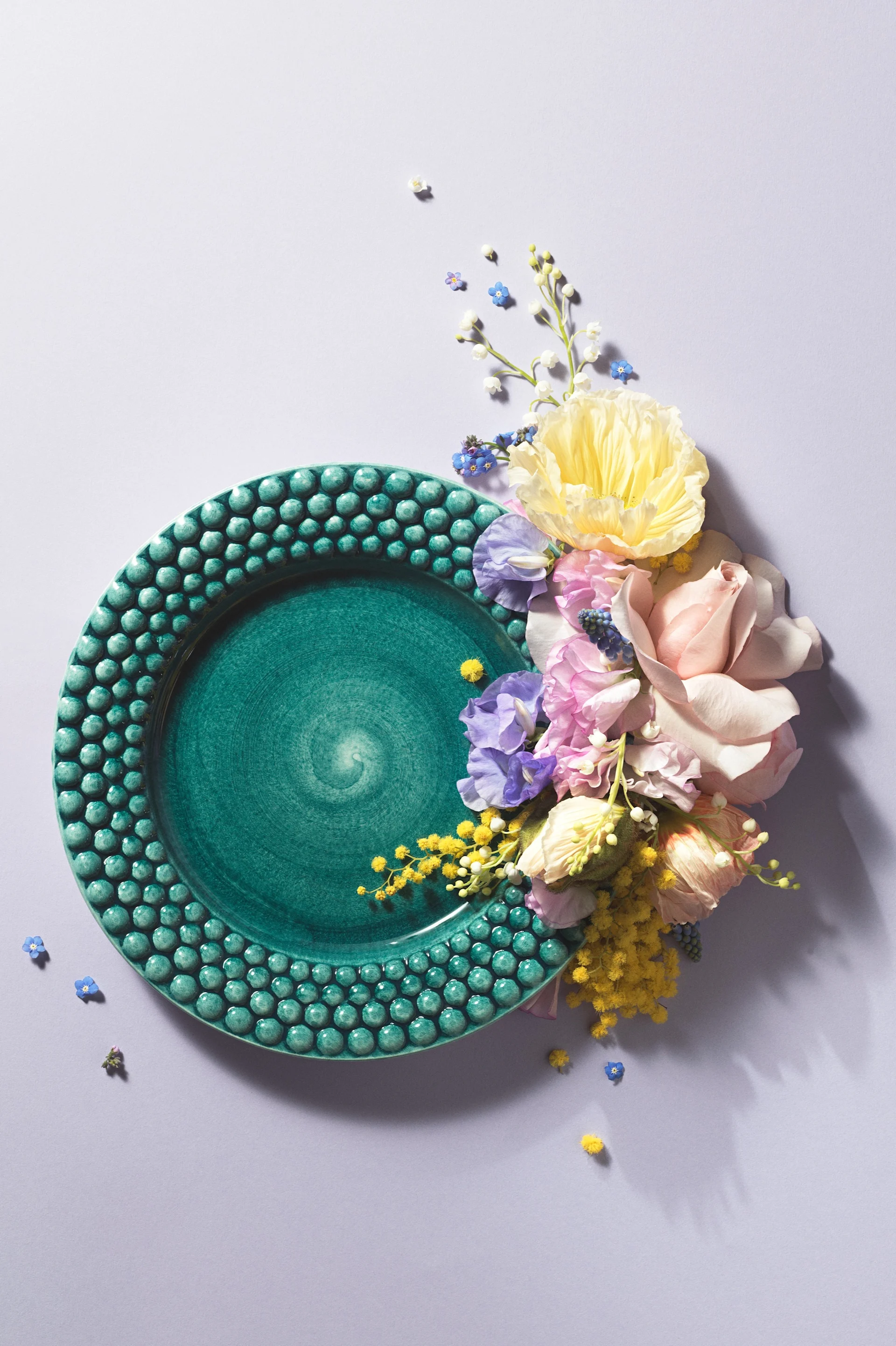 Une assiette de la collection Bubbles en couleur Océan de chez Mateus, mise en scène avec des fleurs pour une photo artistique.