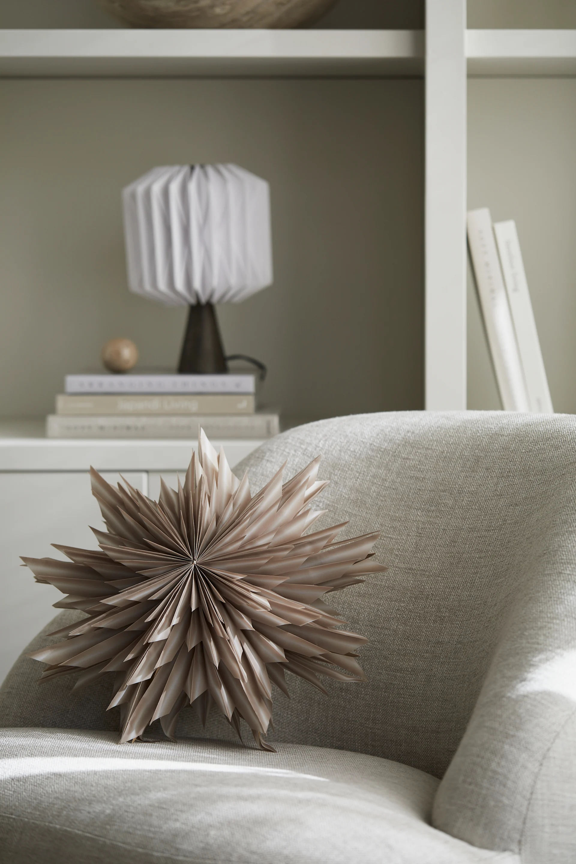 Une lanterne en papier en forme d'étoile de Noël - Helena - de Watt & Veke est posée sur un fauteuil, attendant d'être suspendue.  