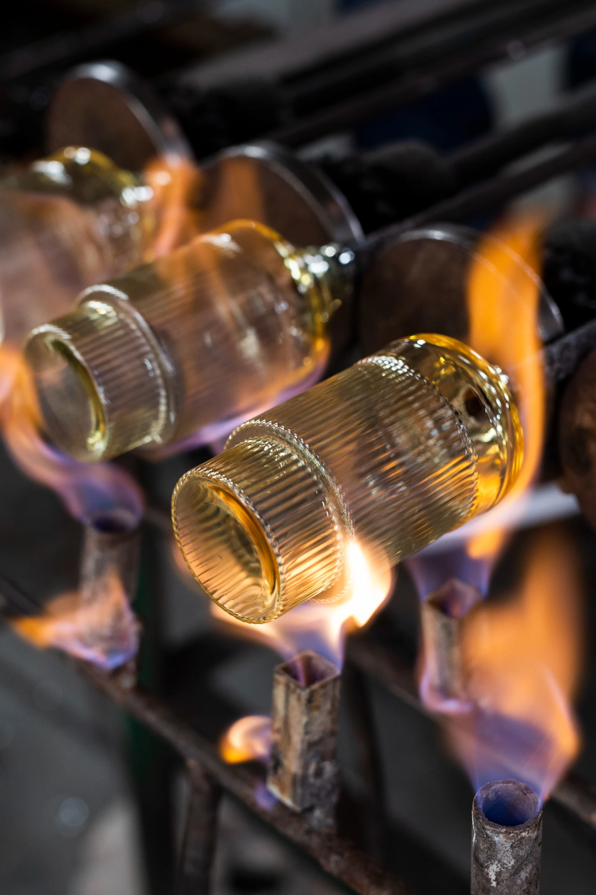 Objets en verre doré nervuré chauffés par des flammes oranges et bleues sur un support métallique.