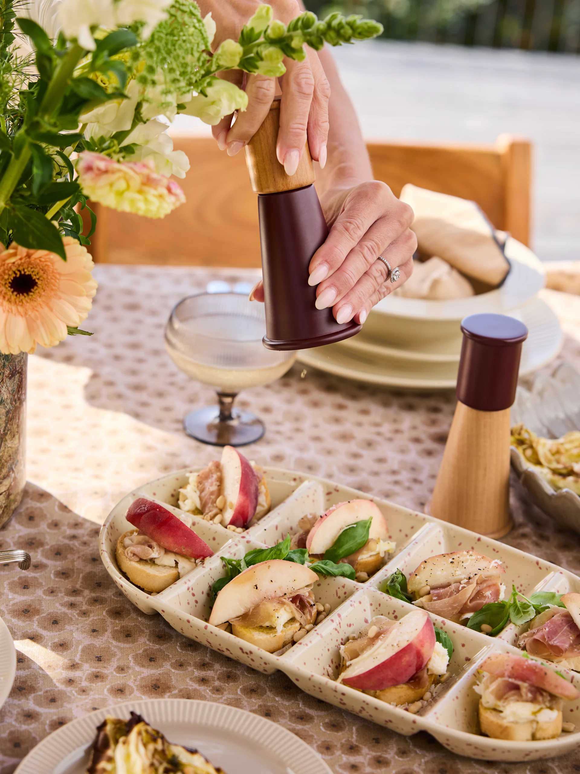 Mains moulant du poivre sur un plateau de crostini avec pêches, prosciutto, fromage, pignons de pin, basilic.