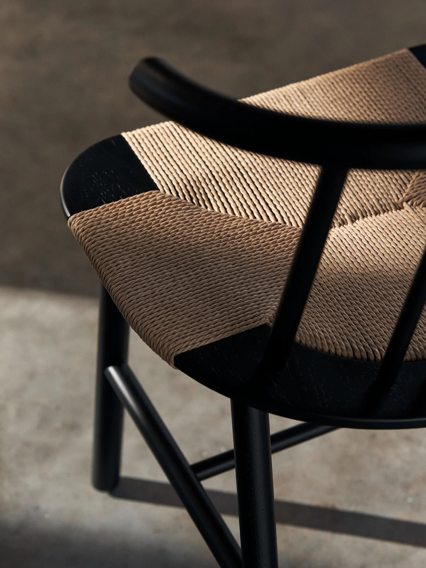 Gros plan d'une chaise en bois noir avec une assise en osier tressé beige clair et un motif diagonal. Des ombres tombent sur l'assise texturée.