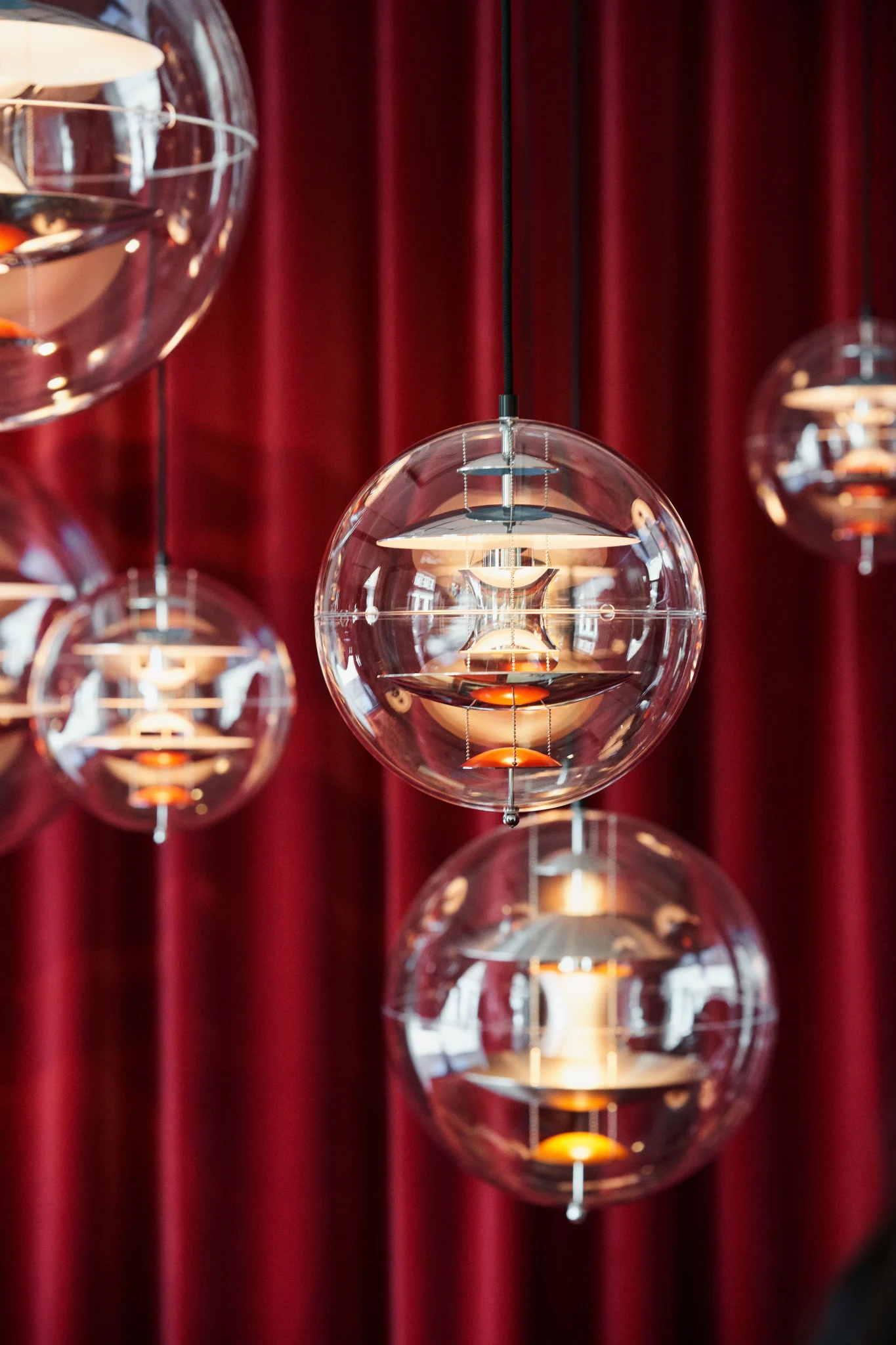 Plusieurs suspensions Globe Glass de Verpan sont suspendues au plafond devant un rideau rouge.