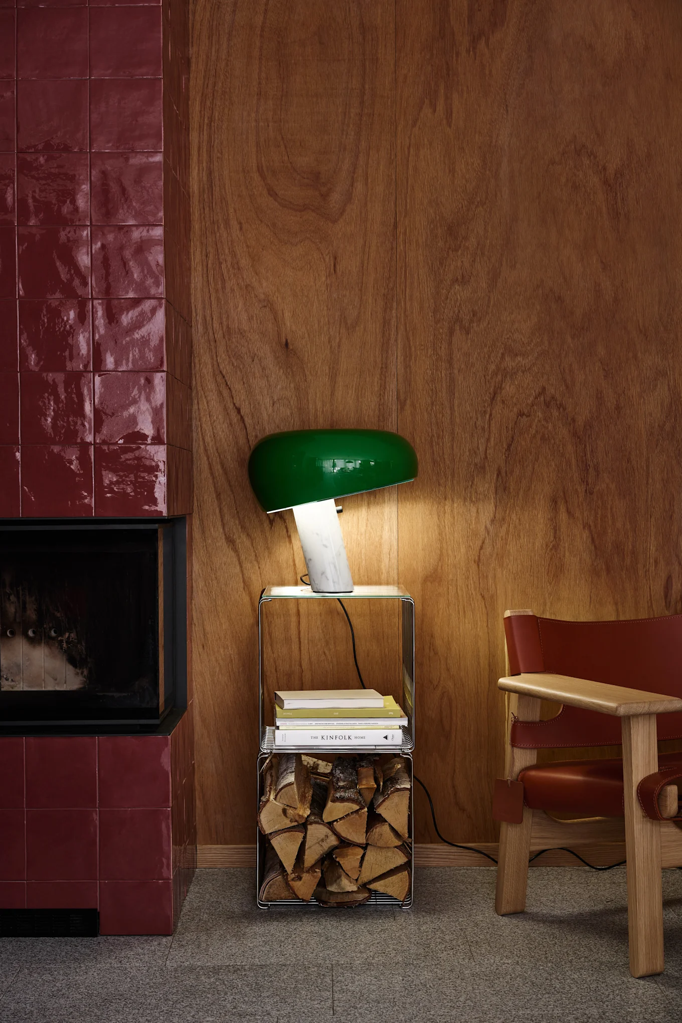 Une chambre à coucher avec une parure de lit à motifs couleur crème, une lampe plissée posée sur une table de chevet en bois et un grand miroir, le tout sur fond de papier peint à motifs de feuillage.