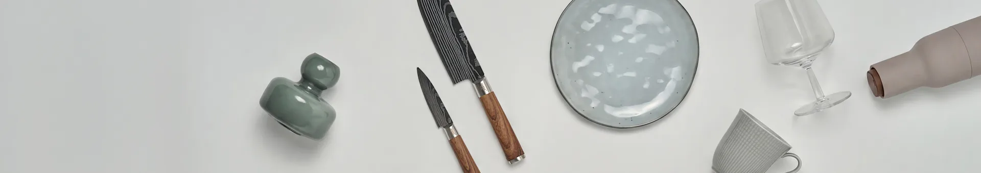 Divers articles de cuisine et de table, y compris un vase vert, deux couteaux, une assiette mouchetée, un verre à vin, une bouteille beige et une tasse à motifs.
